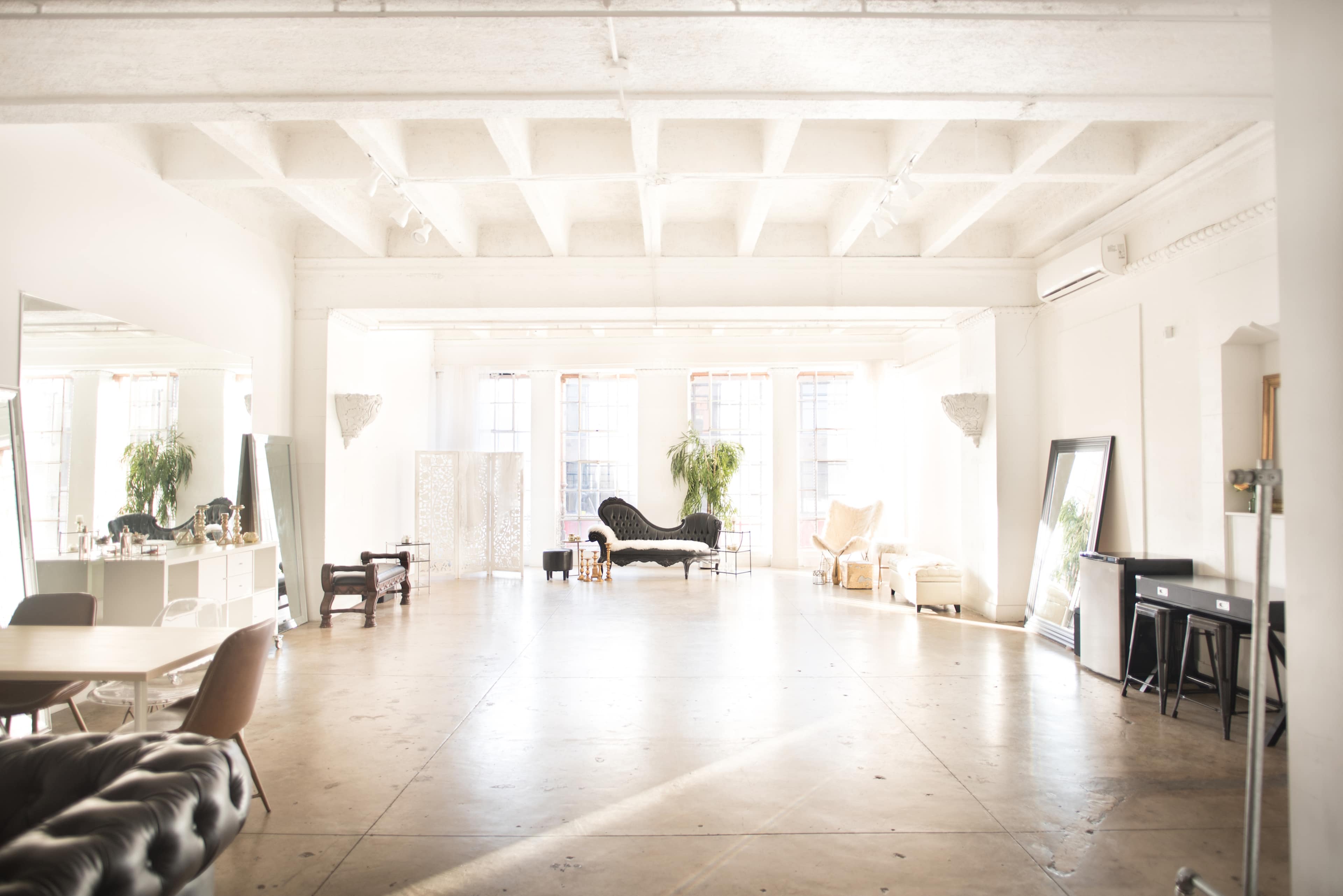 A spacious, well-lit room with large windows, various furnishings, and decorative plants.
