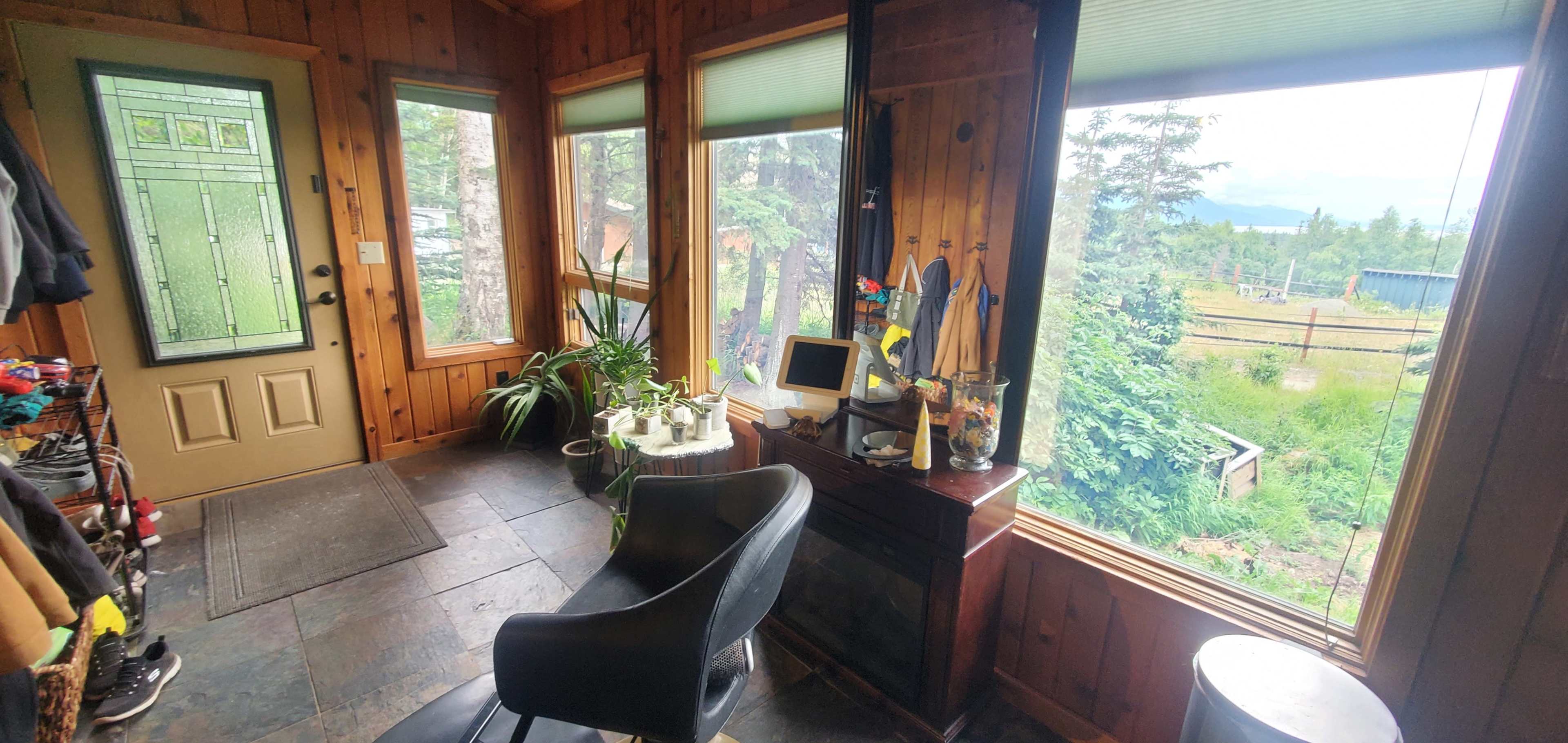 A wooden-paneled entryway with large windows, a chair, and plants, overlooking a green outdoor area.