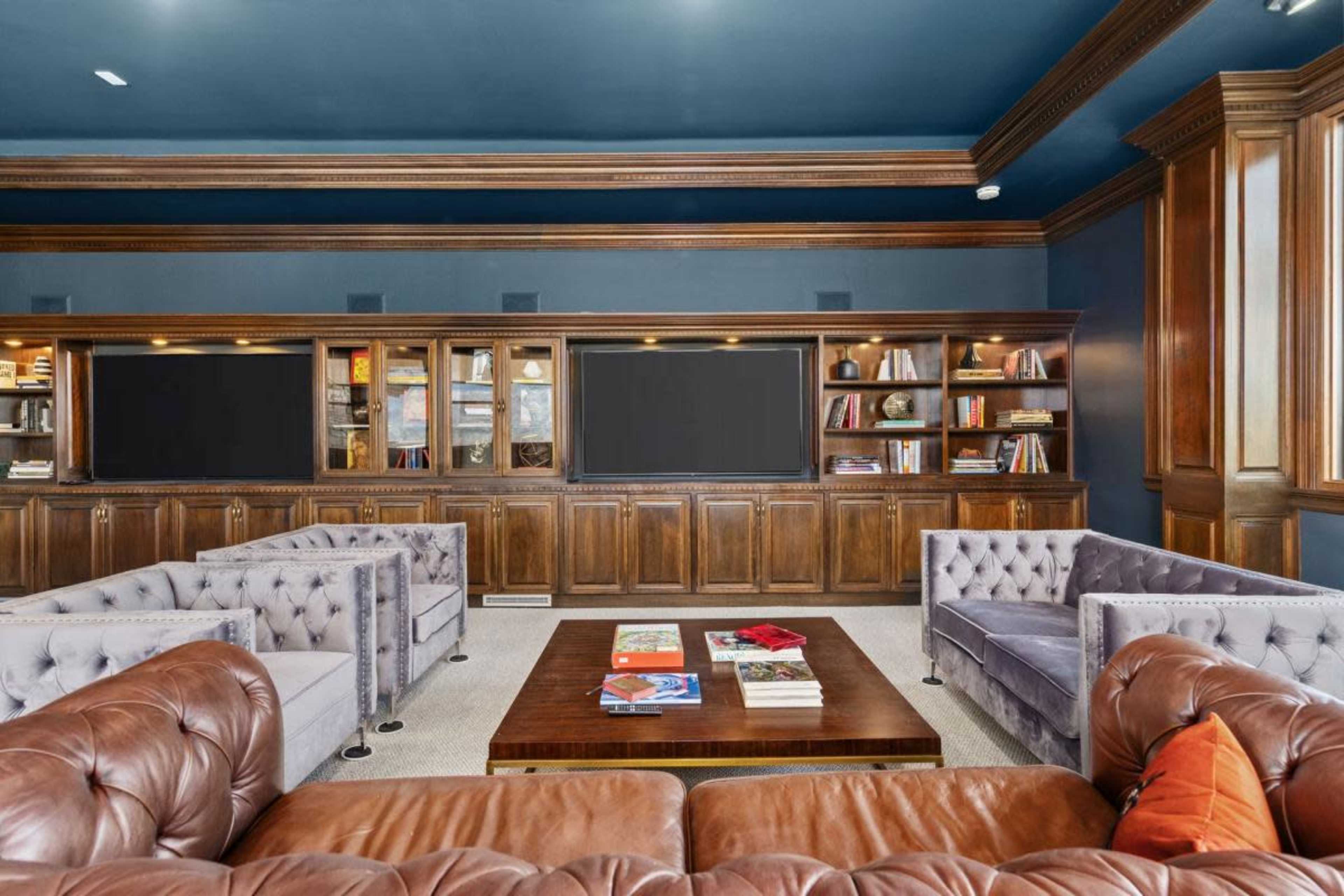 A spacious library features elegant wooden bookshelves, a central coffee table, and plush seating areas with tufted sofas.