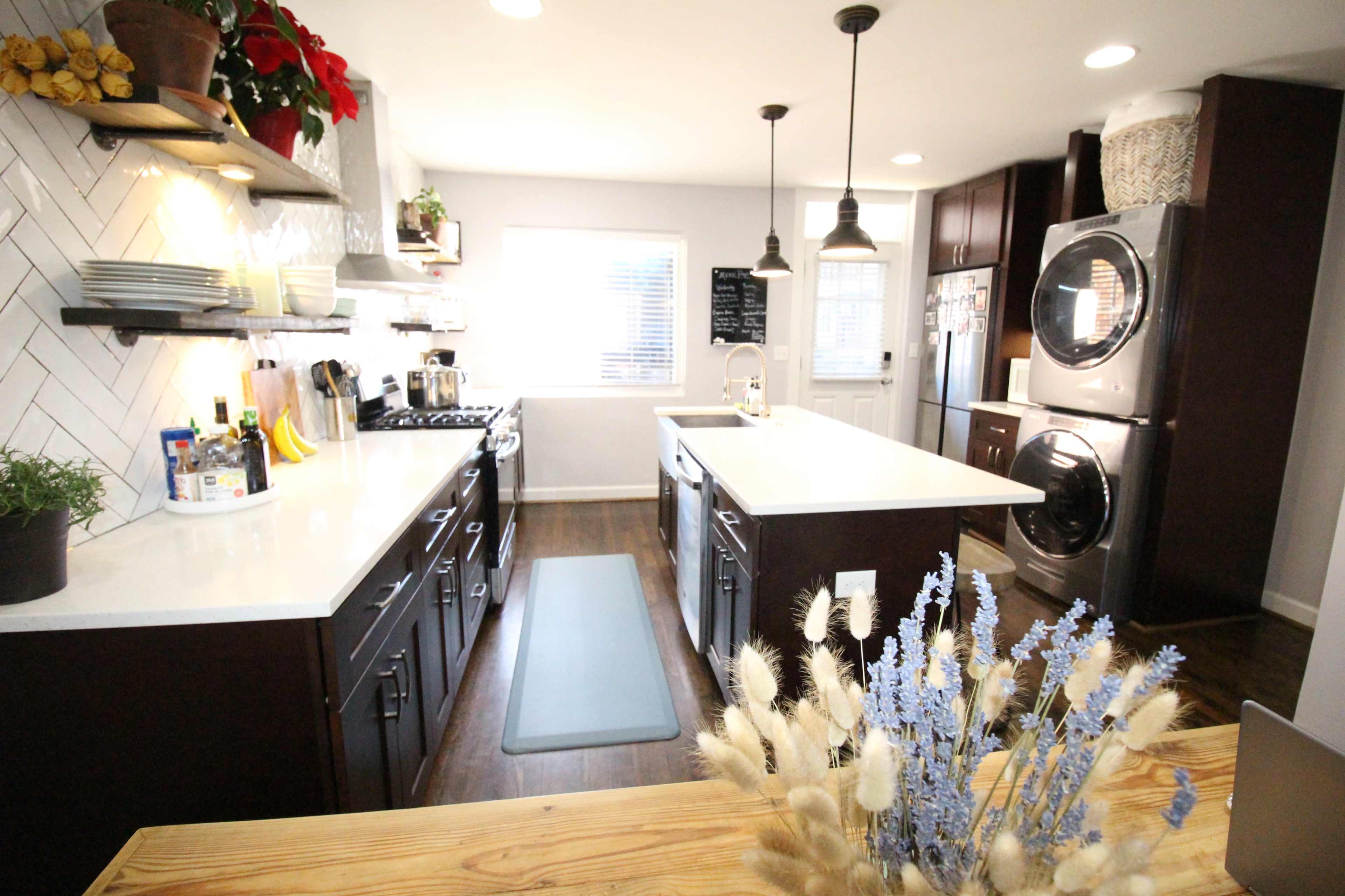 A modern kitchen featuring dark cabinets, a large island with a white countertop, and stainless steel appliances.