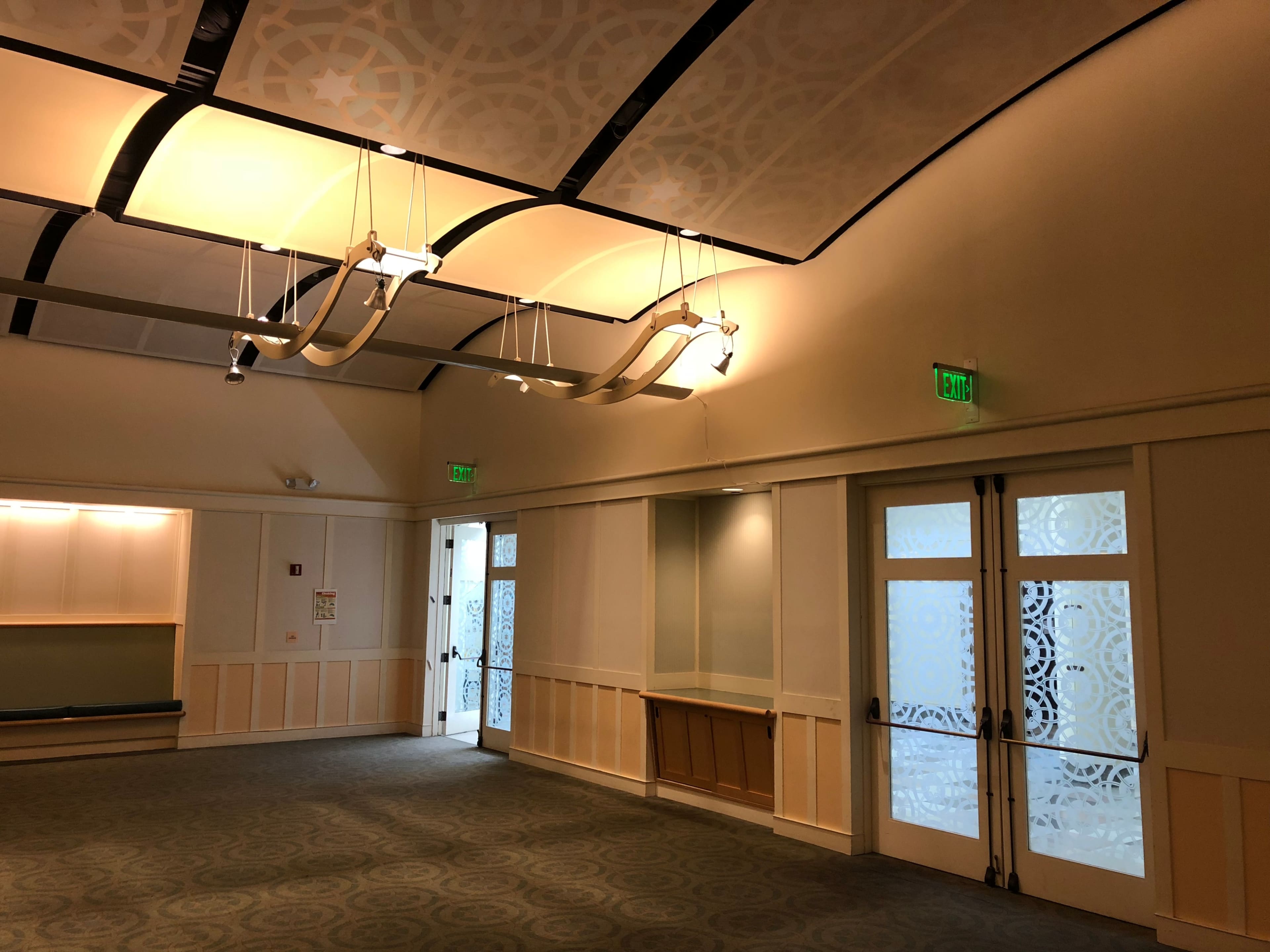A spacious interior of a room with a textured ceiling, two exit doors, and green exit signs.