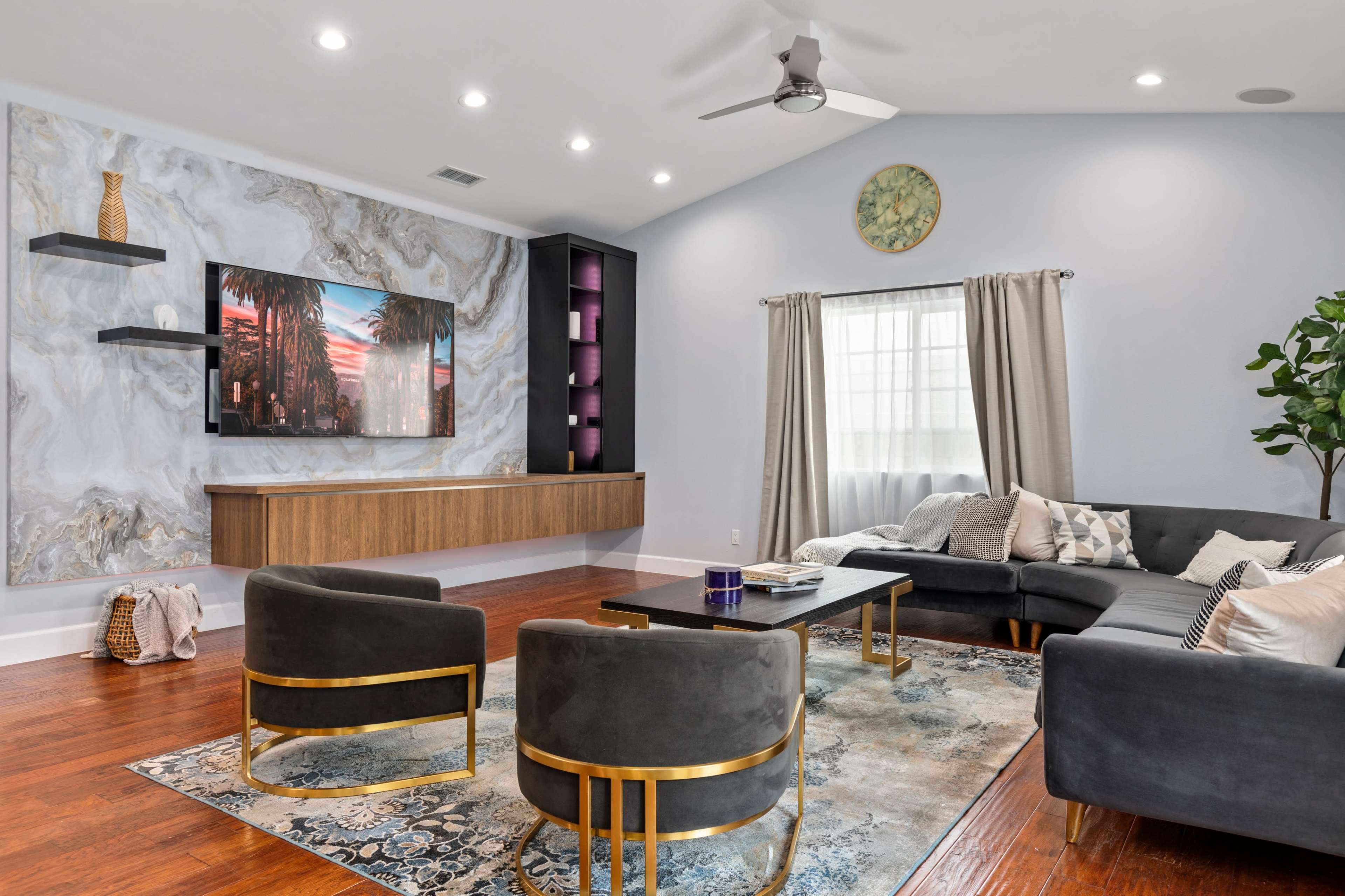 A modern living room with a large wall-mounted TV, a stylish sectional sofa, and a decorative area rug on hardwood flooring.