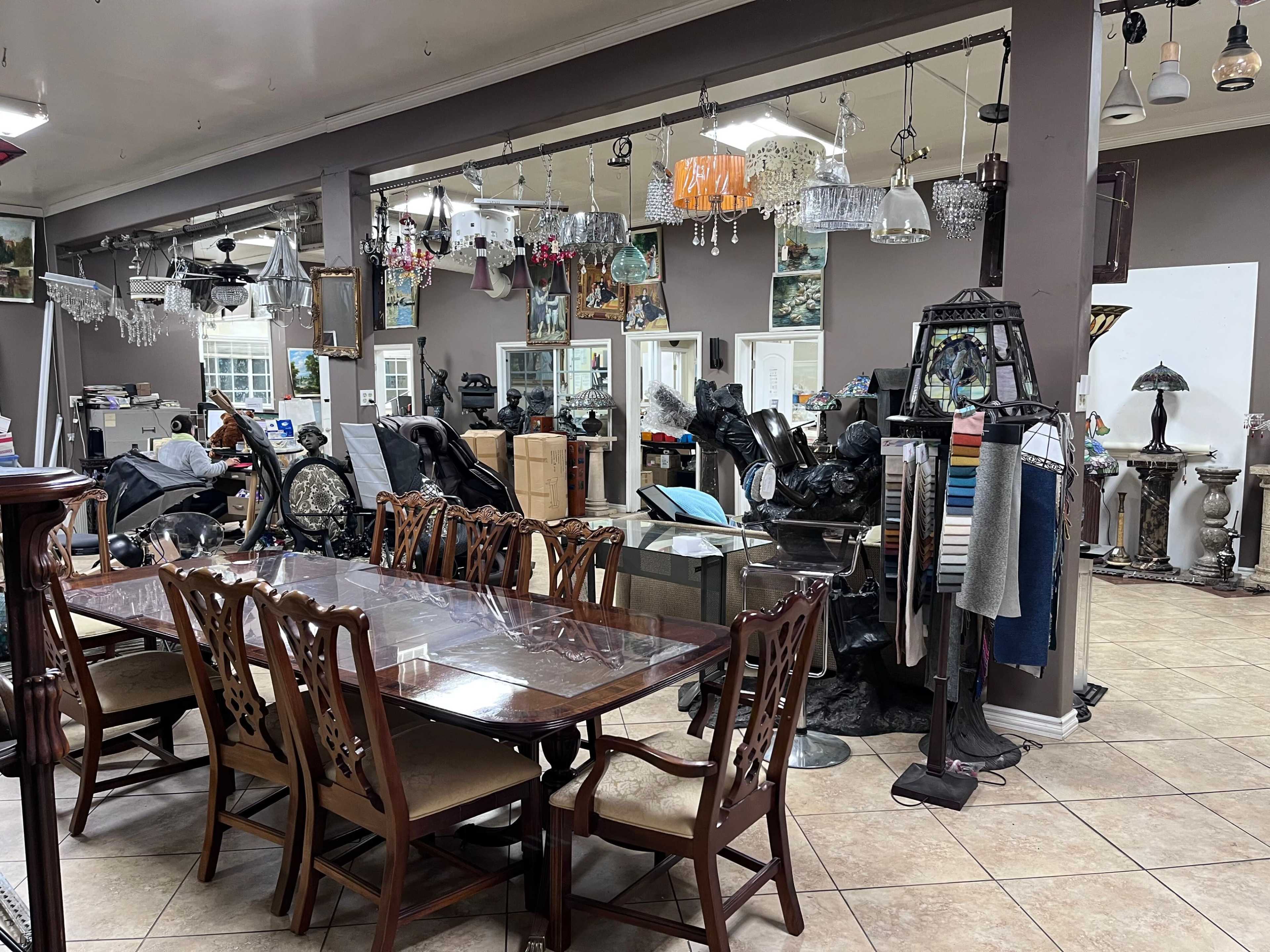 The image shows a cluttered interior of a furniture store with a dining table, various light fixtures, and assorted home decor items.