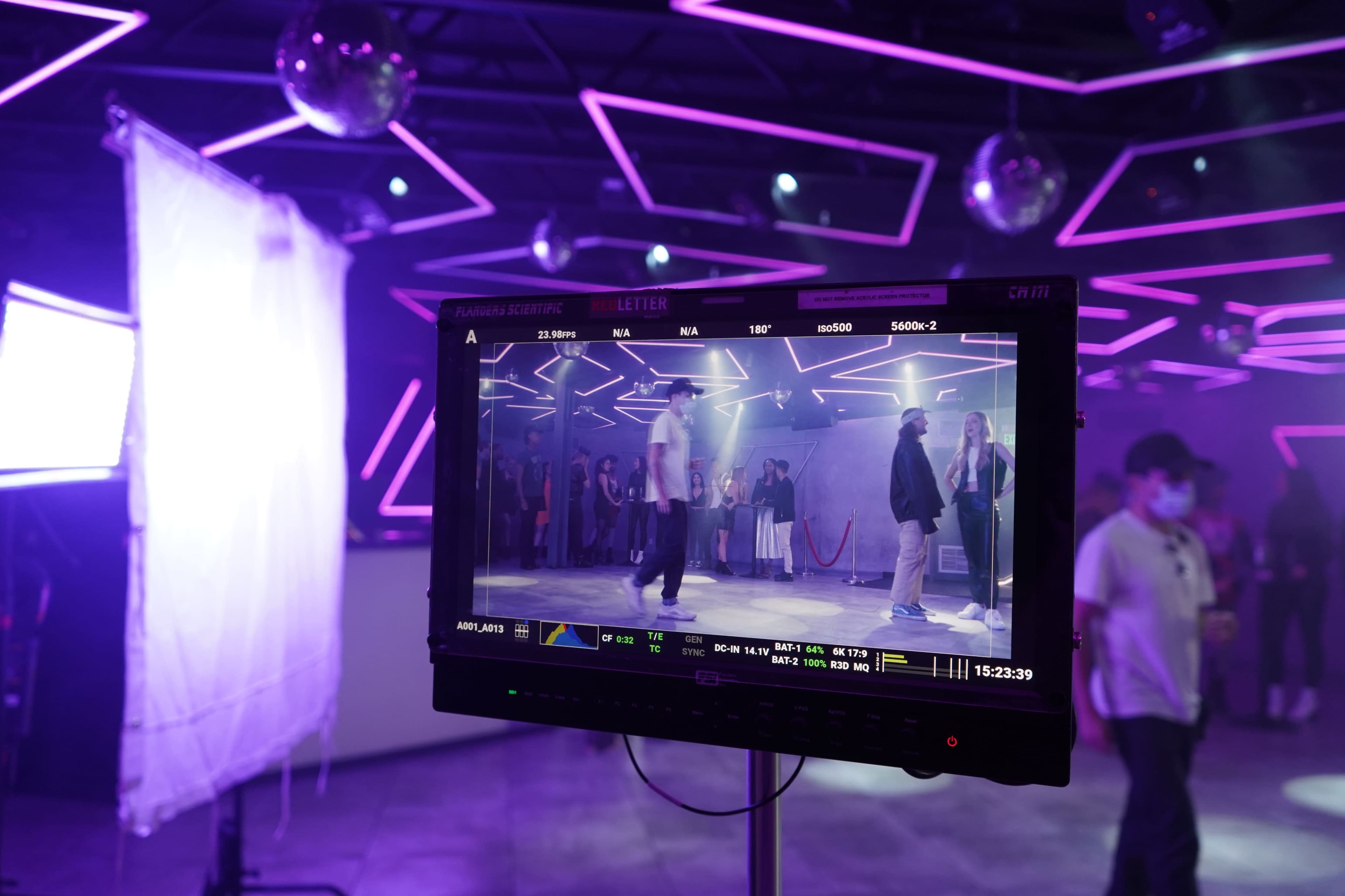 A monitor displays a scene of performers dancing in a venue with purple lighting and disco balls.