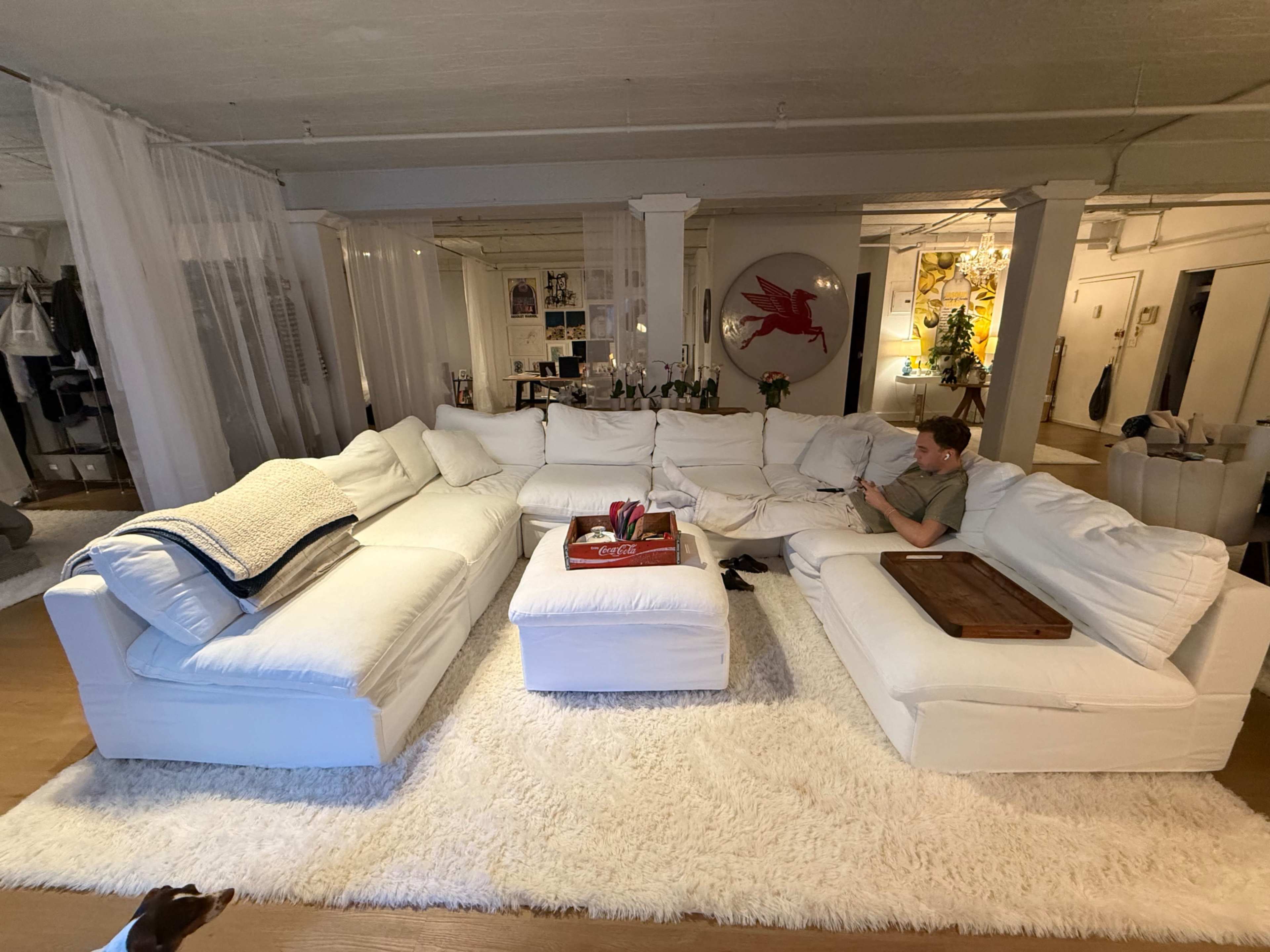 A large white sectional sofa occupies a spacious room, with a man sitting on it and a round table in the center.