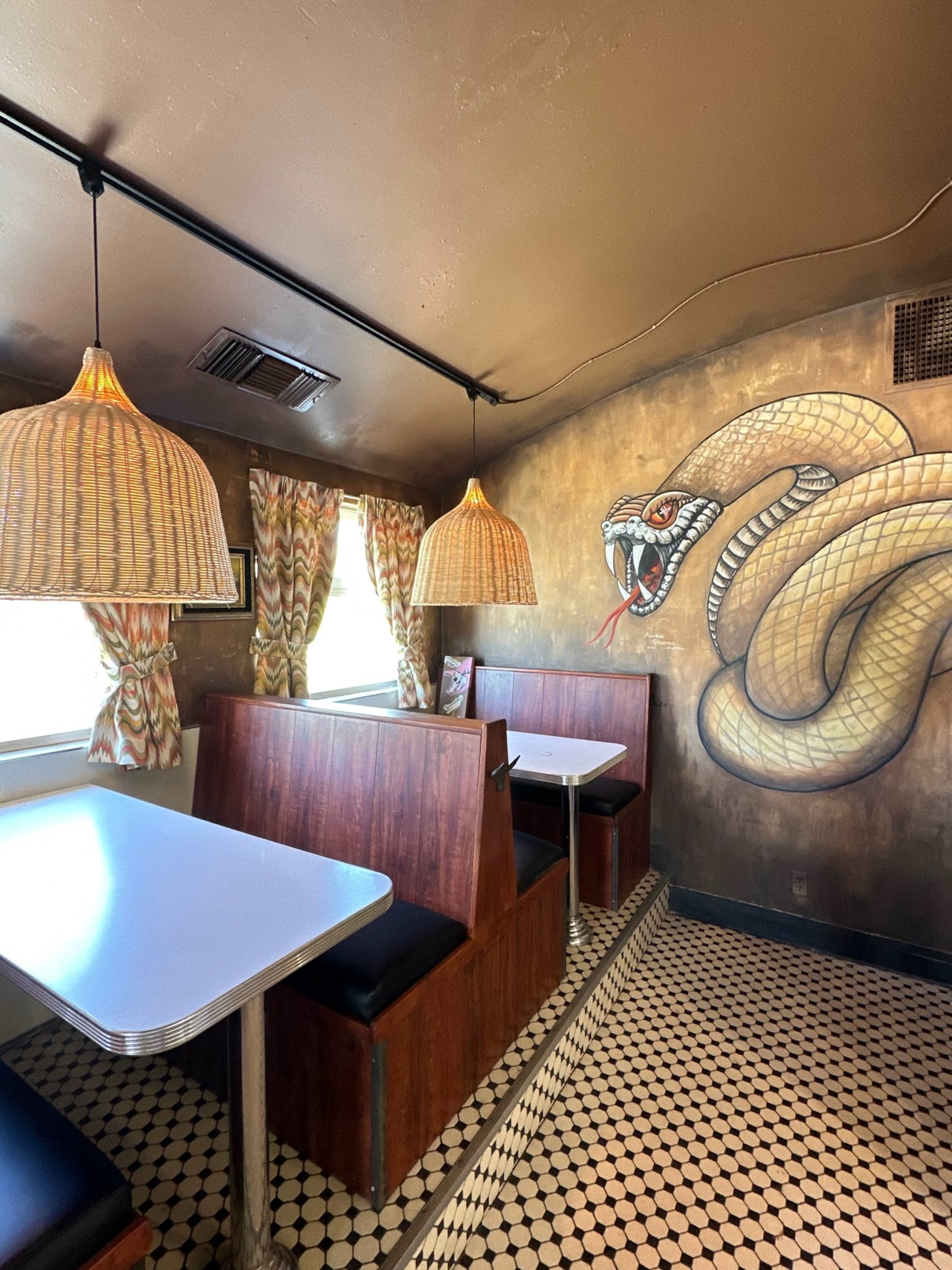 The image shows a small diner interior featuring two booths, wicker light fixtures, and a large snake mural on the wall.