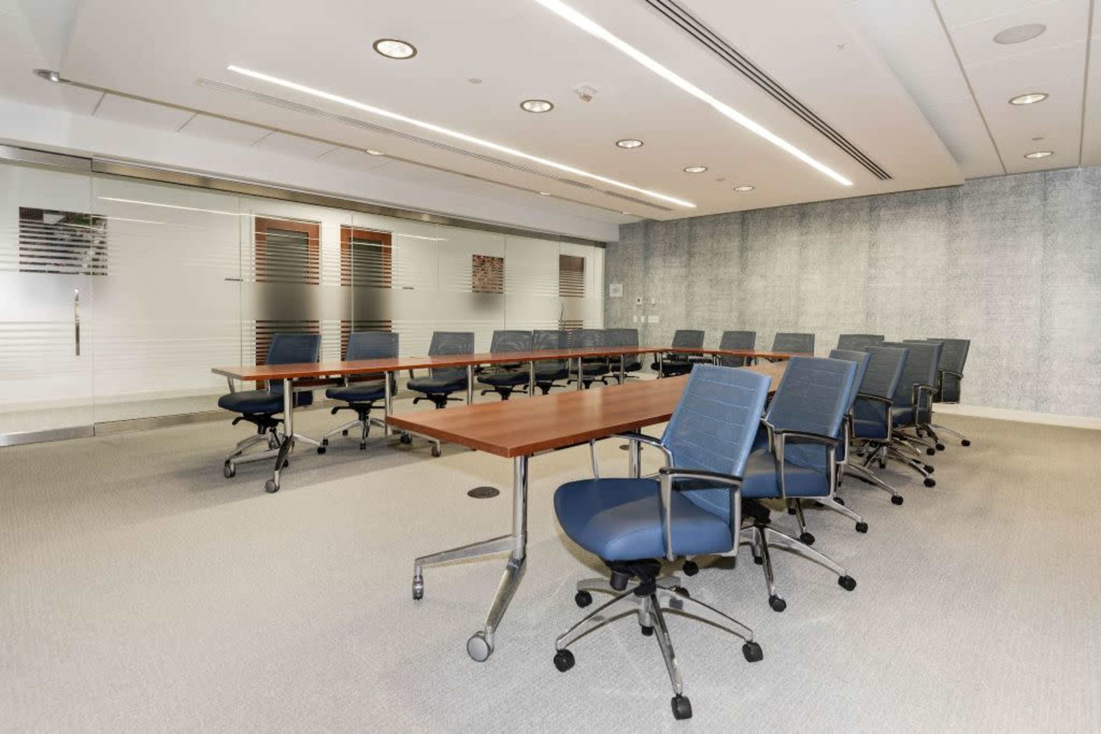A modern conference room features a long wooden table surrounded by blue ergonomic chairs, with glass panels and a textured wall.