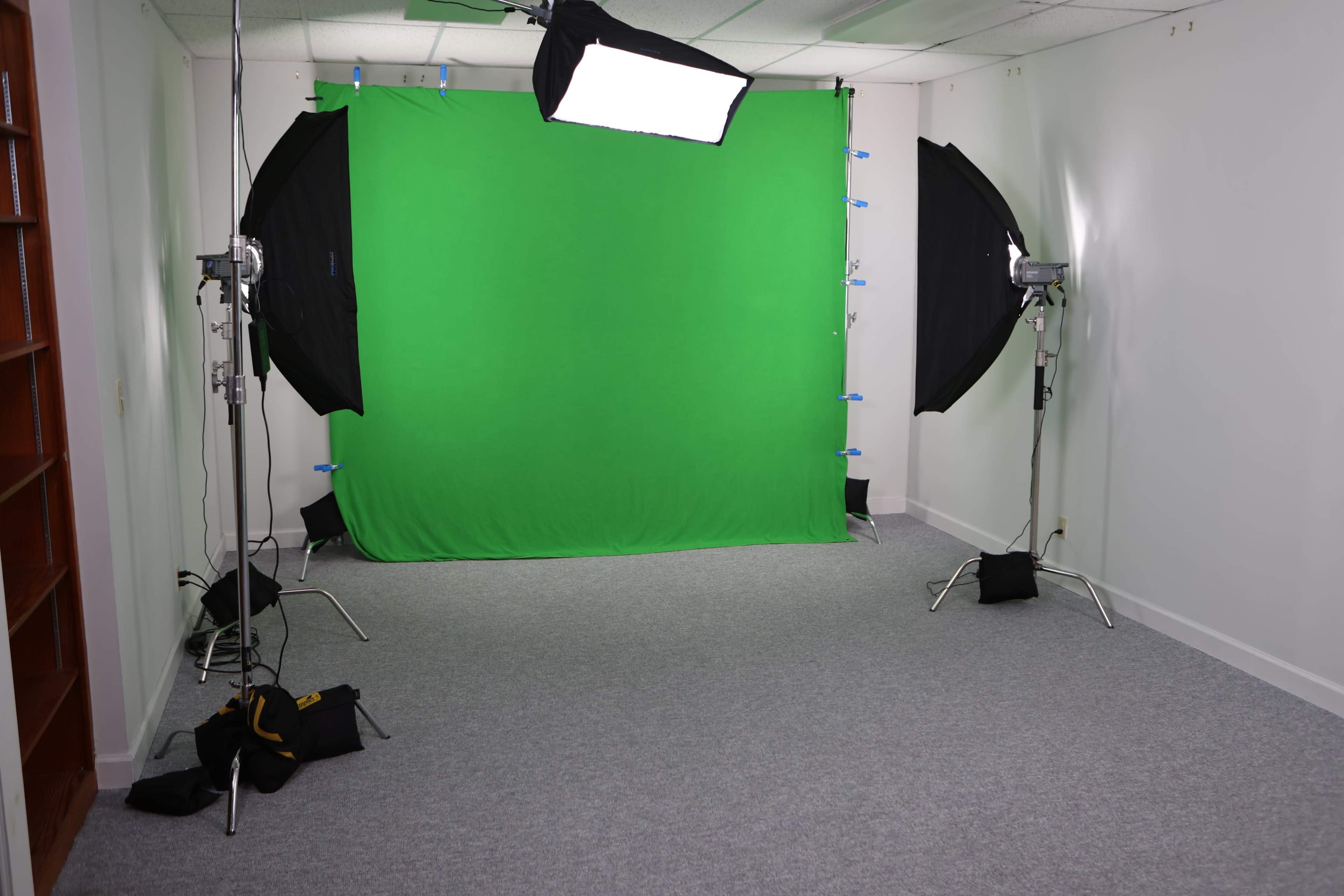 The image shows a photo studio with a green backdrop, two softbox lights on either side, and soft flooring.