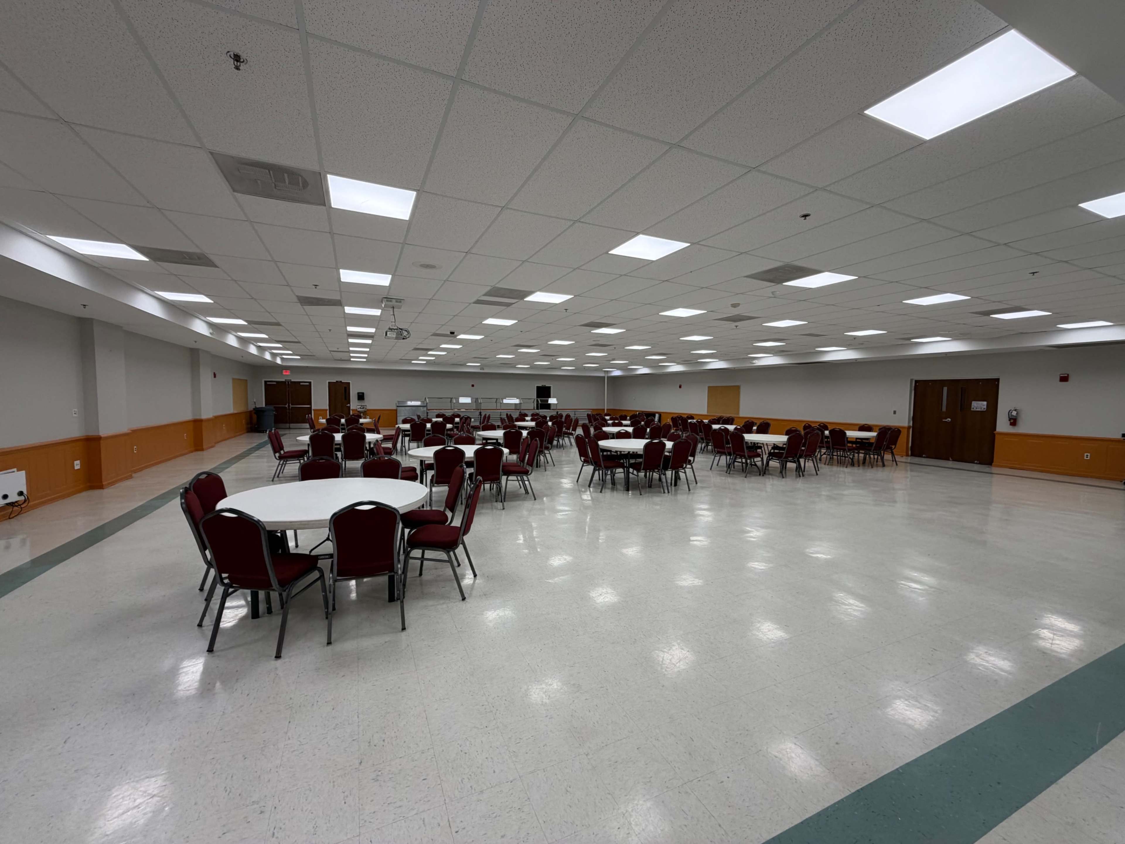 The image shows a large, empty banquet hall arranged with round tables and red chairs.