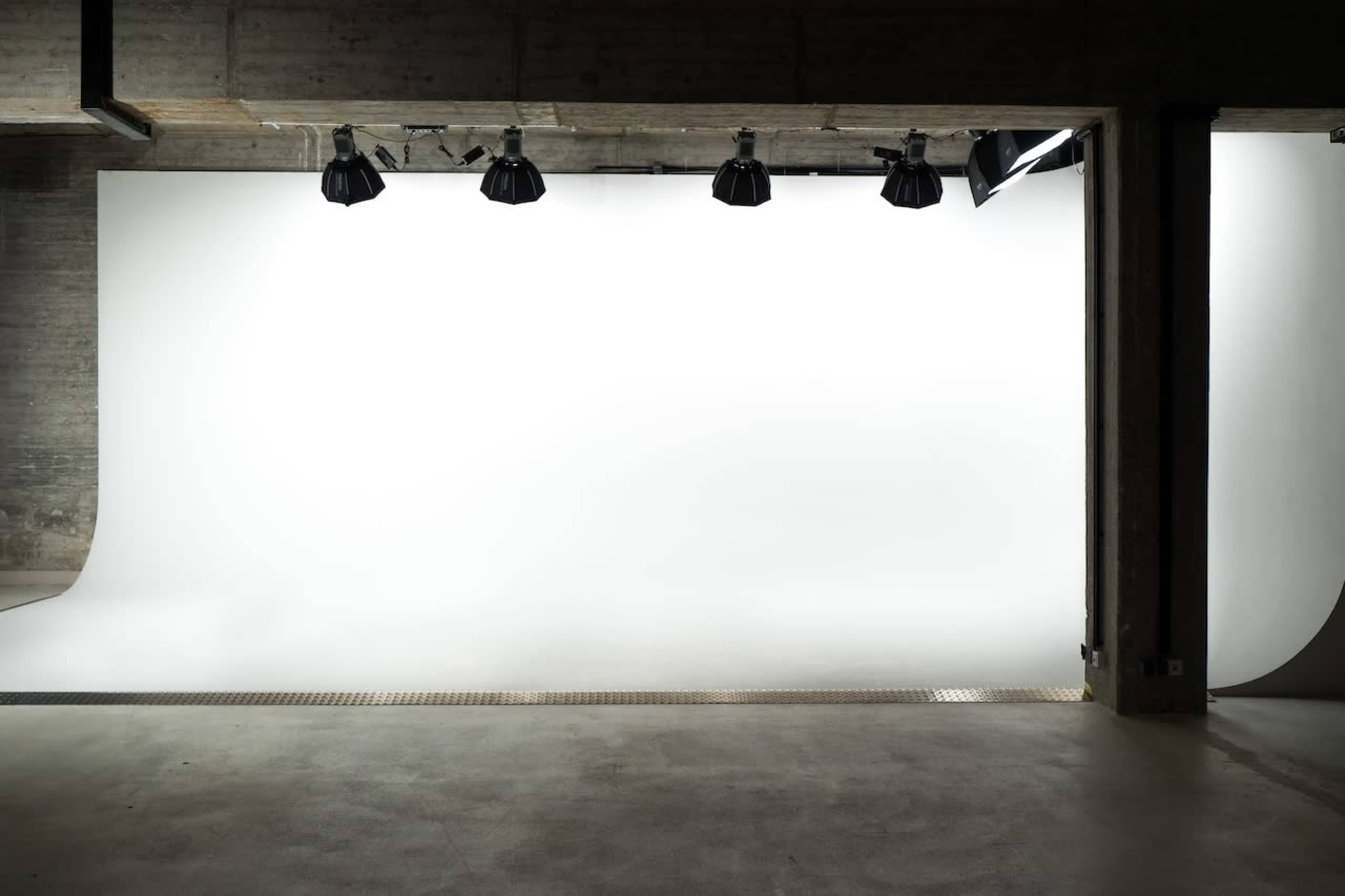 The image shows a spacious studio with a seamless white backdrop under studio lights.