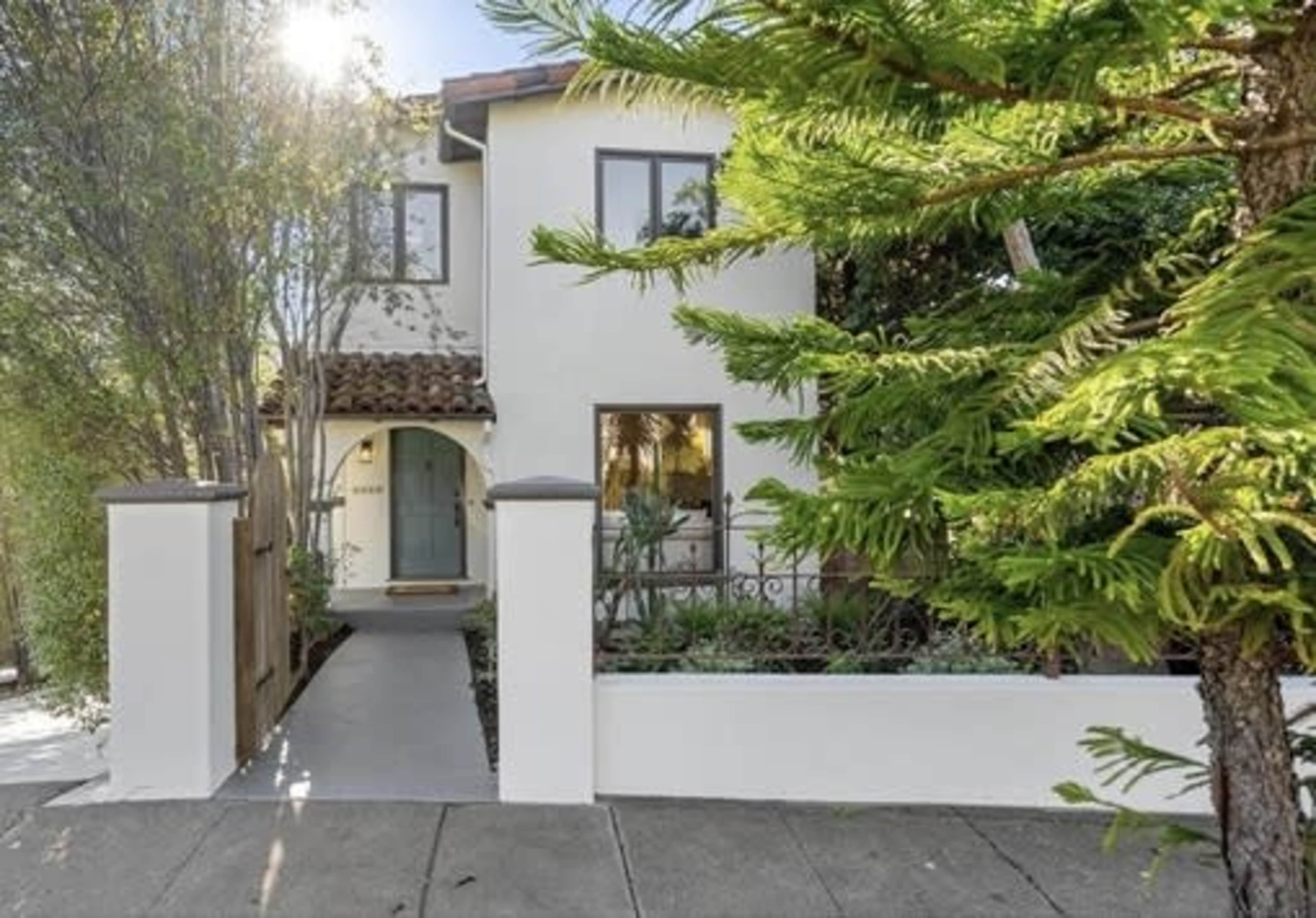 A two-story white house with a tiled roof, surrounded by greenery and a pathway leading to the entrance.