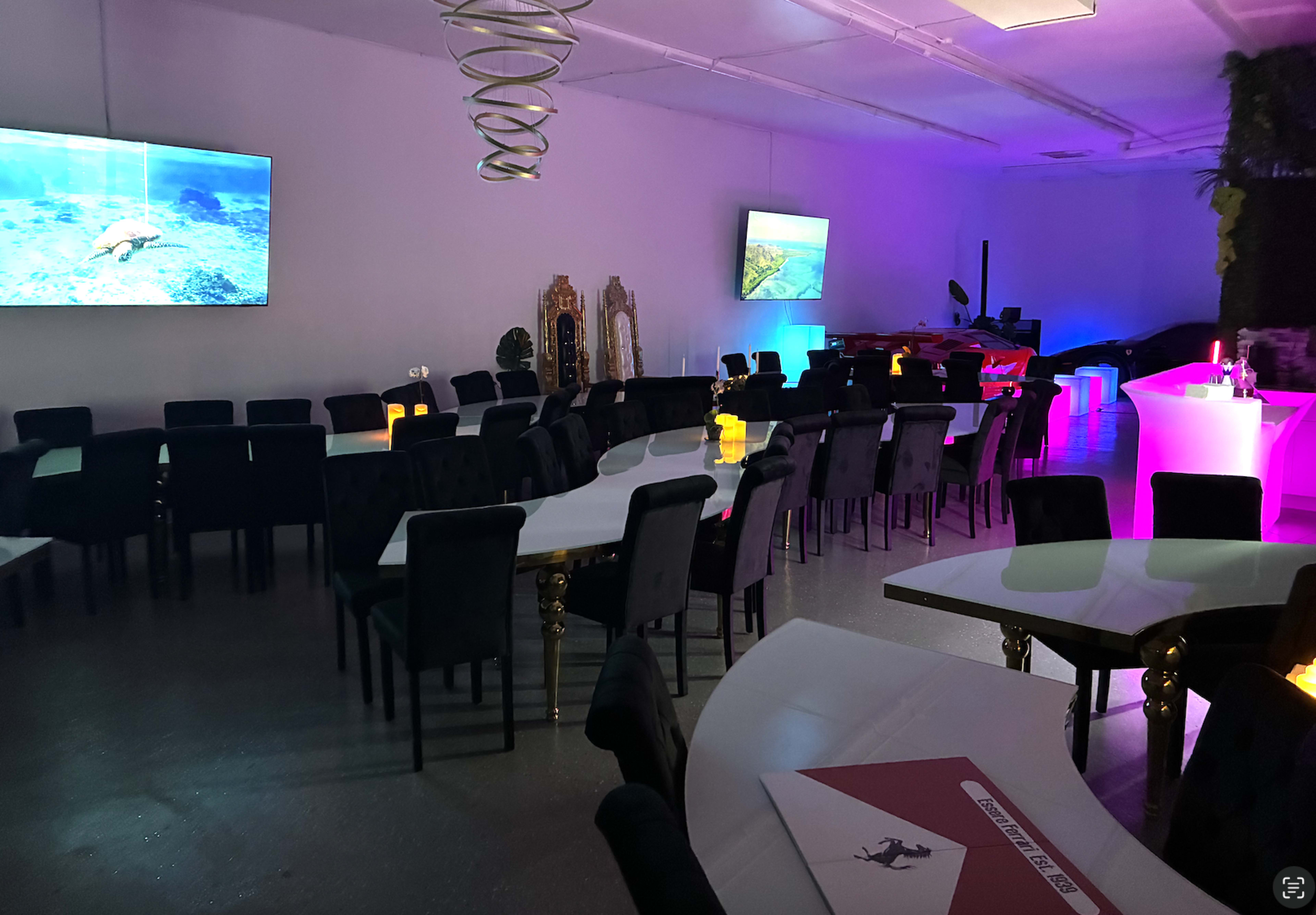 The image shows a spacious, modern dining area with tables arranged in a U-shape, featuring decorative lighting and two large screens displaying underwater scenes.