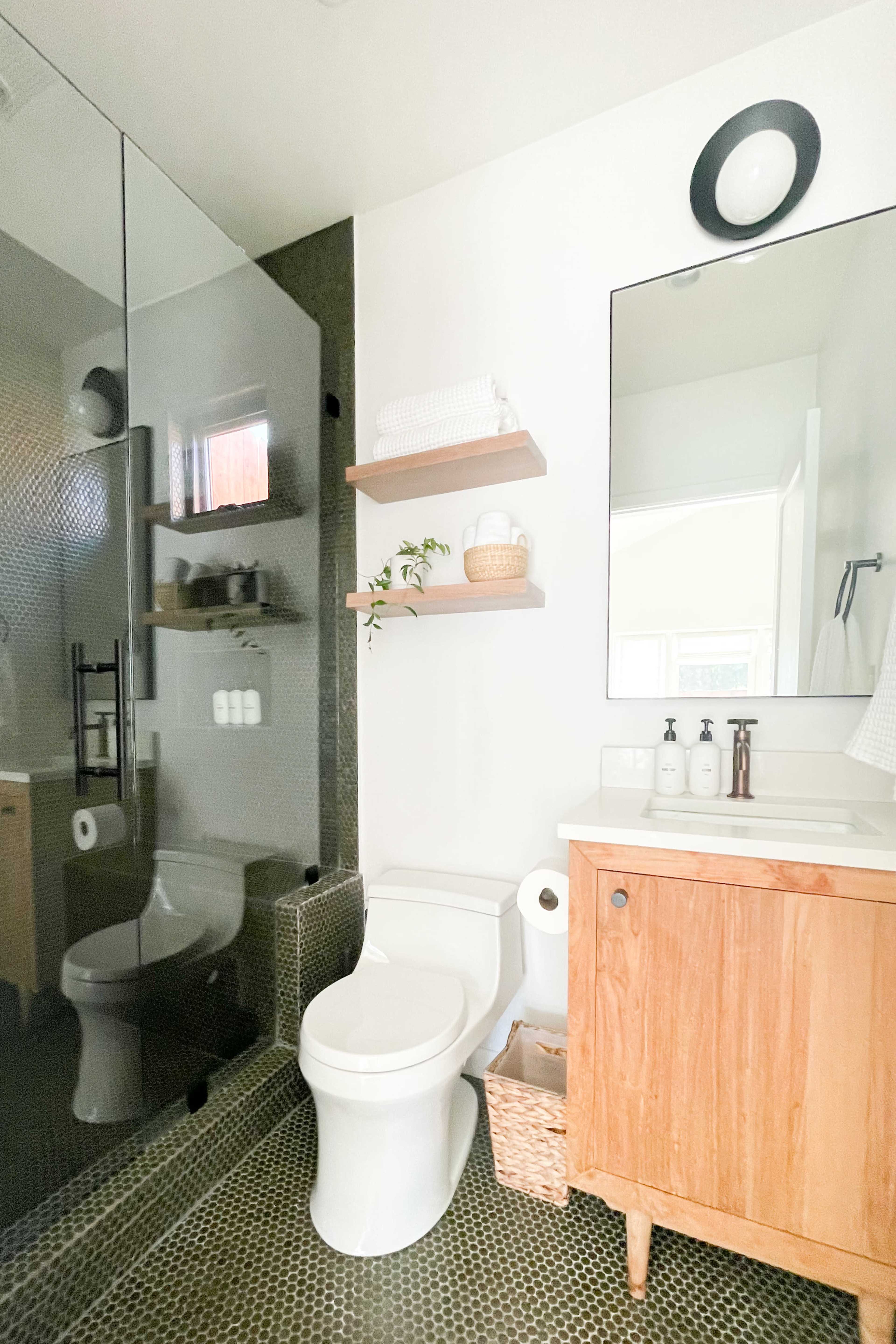 A modern bathroom featuring a glass shower, a toilet, a wooden vanity with a sink, and shelves with decorative items.