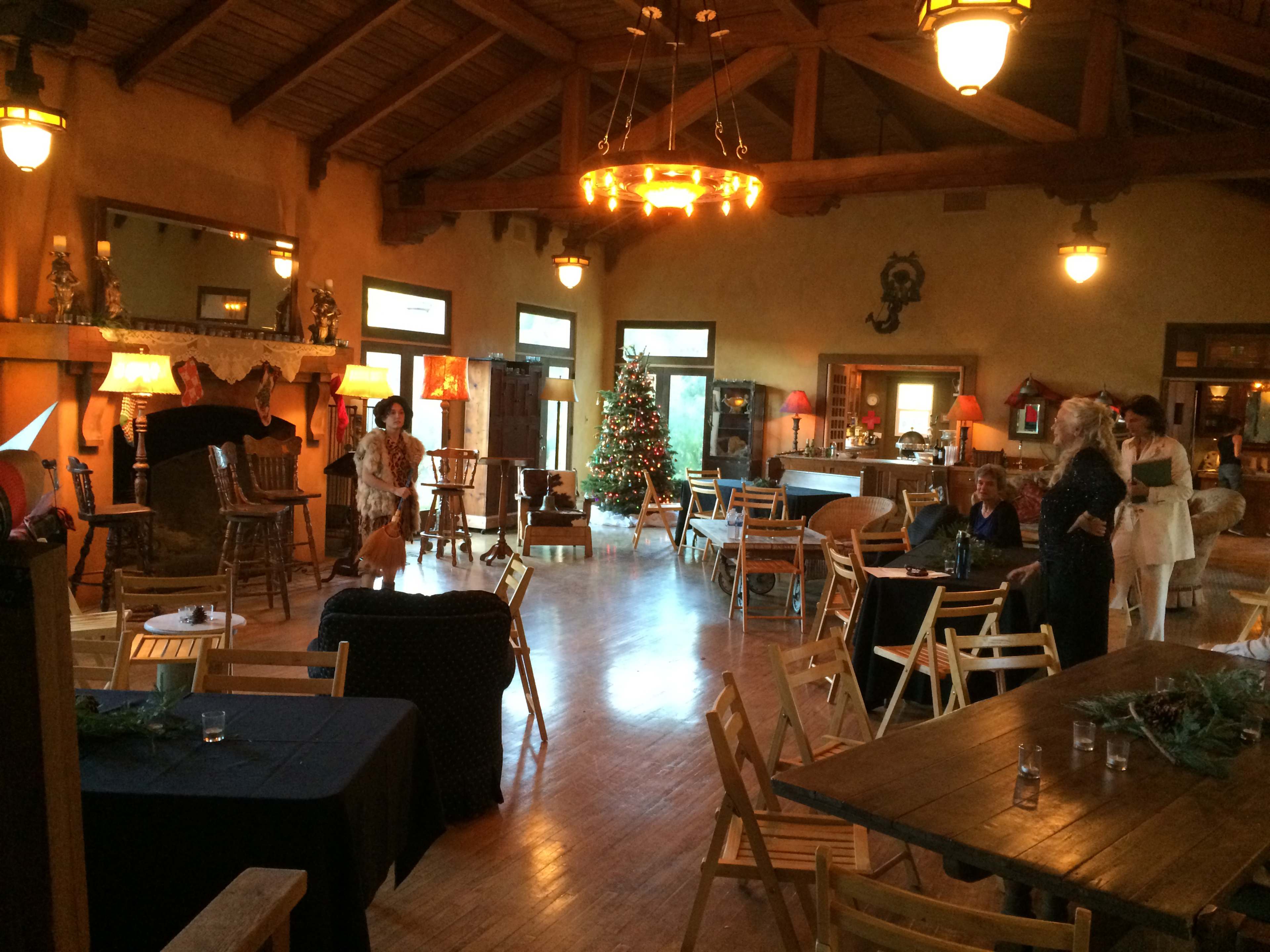 A spacious, decorated room with wooden beams, a Christmas tree in one corner, and several tables and chairs arranged for an event.
