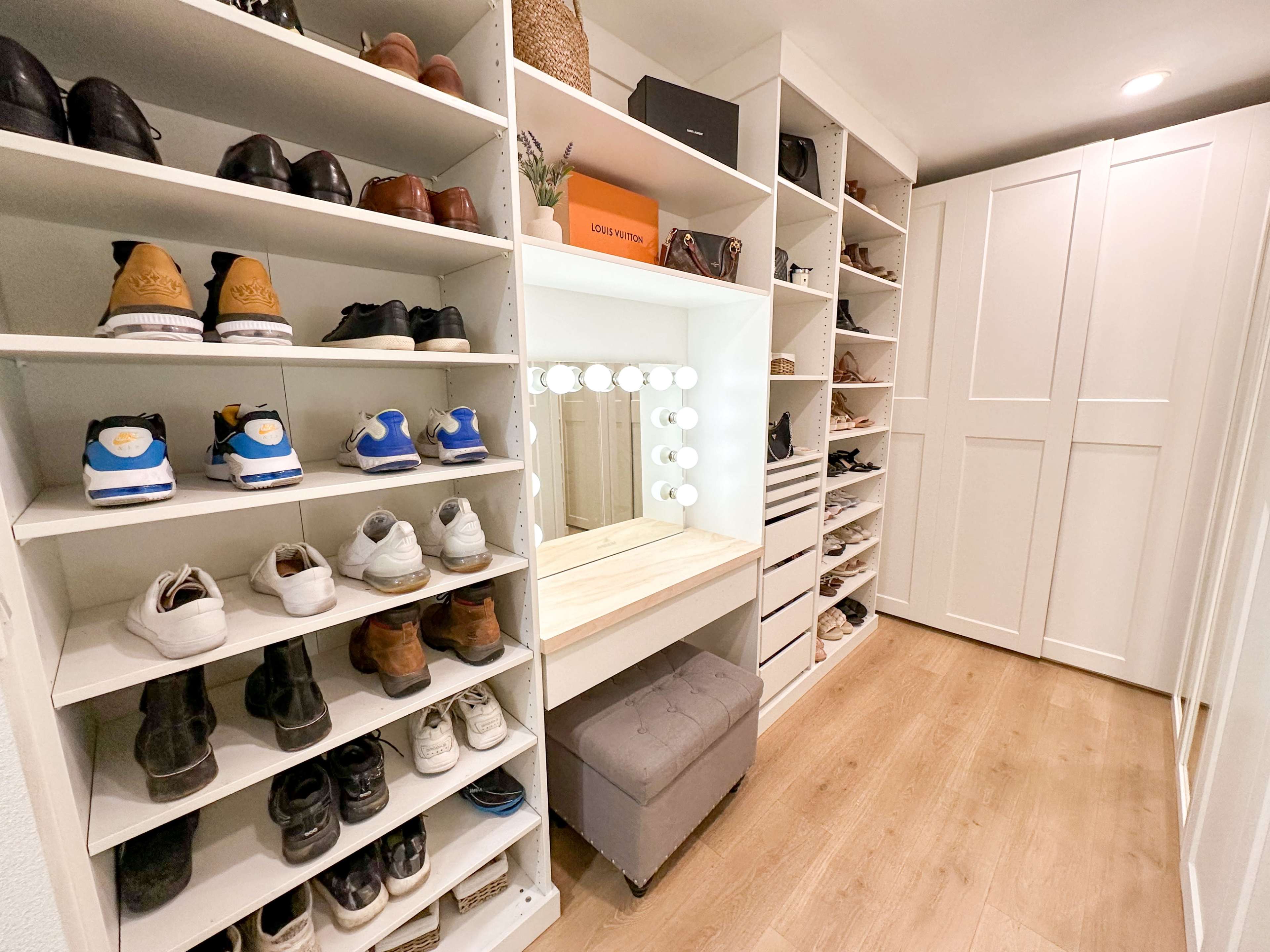 A well-organized shoe storage area with shelves on either side and a vanity mirror at the center, surrounded by various types of shoes and a stool.