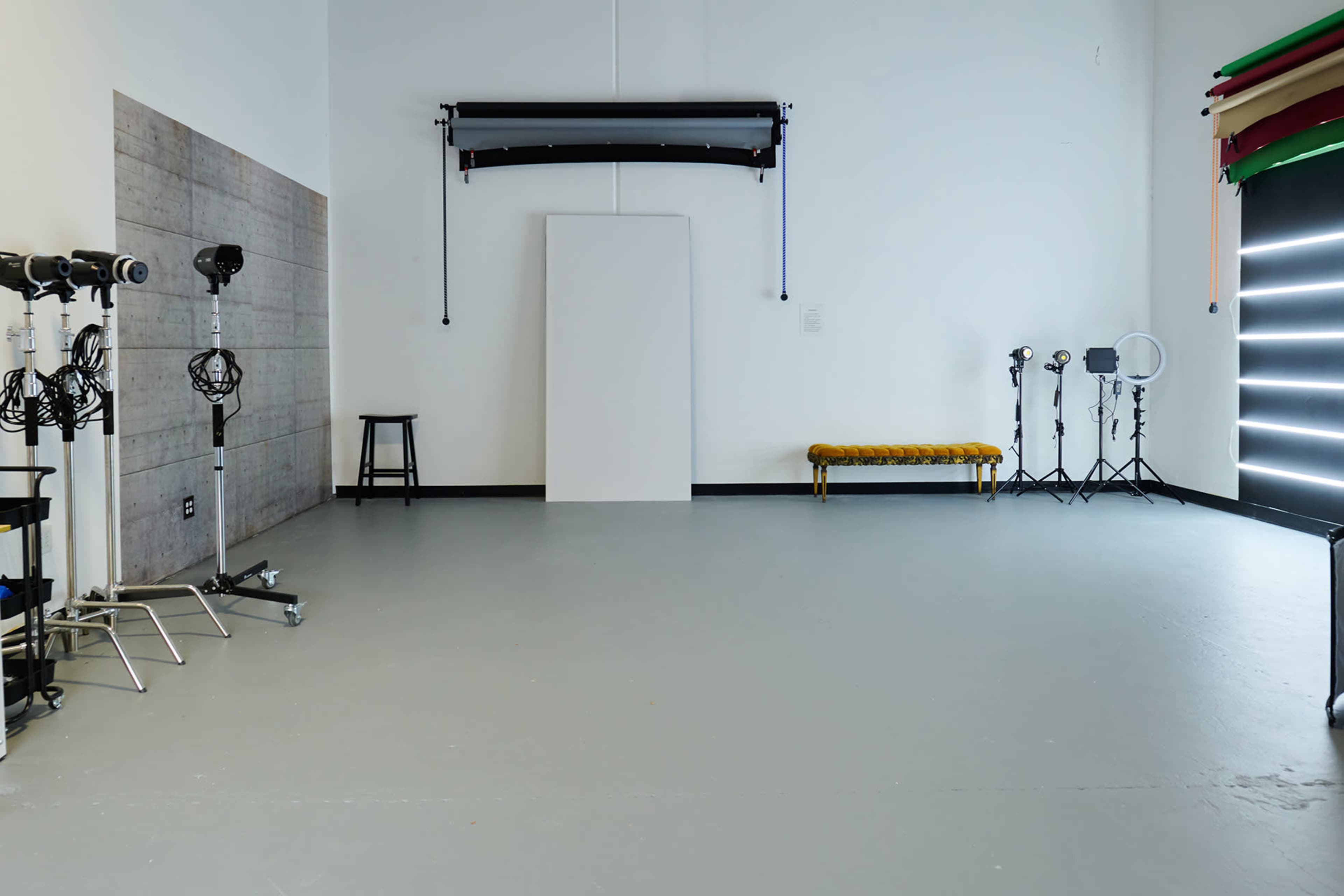 The image shows a spacious photography studio with various lighting equipment, a backdrop, and a decorative bench against a plain wall.