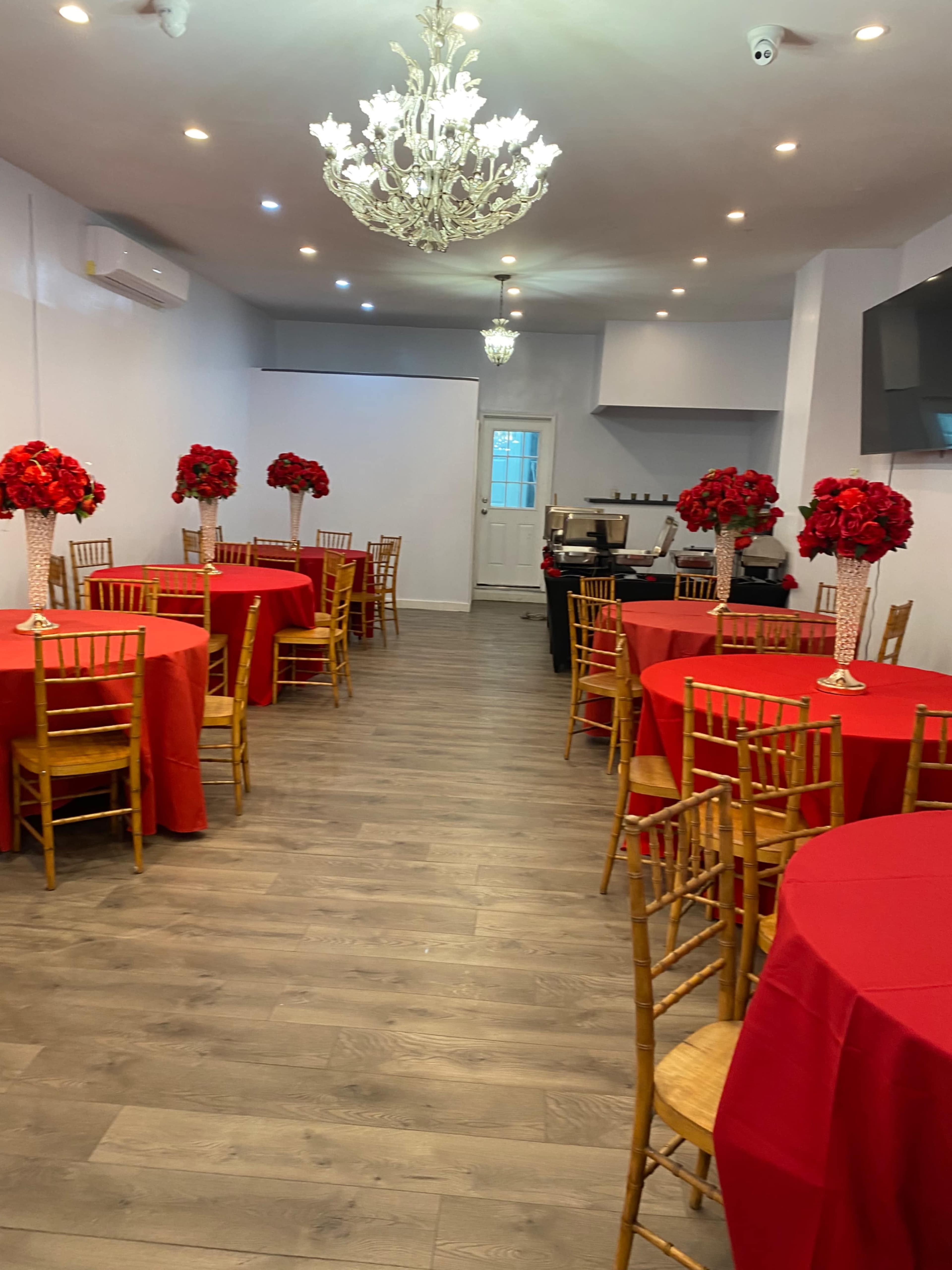 A banquet hall with red tablecloths, golden chairs, and floral centerpieces, illuminated by a chandelier.