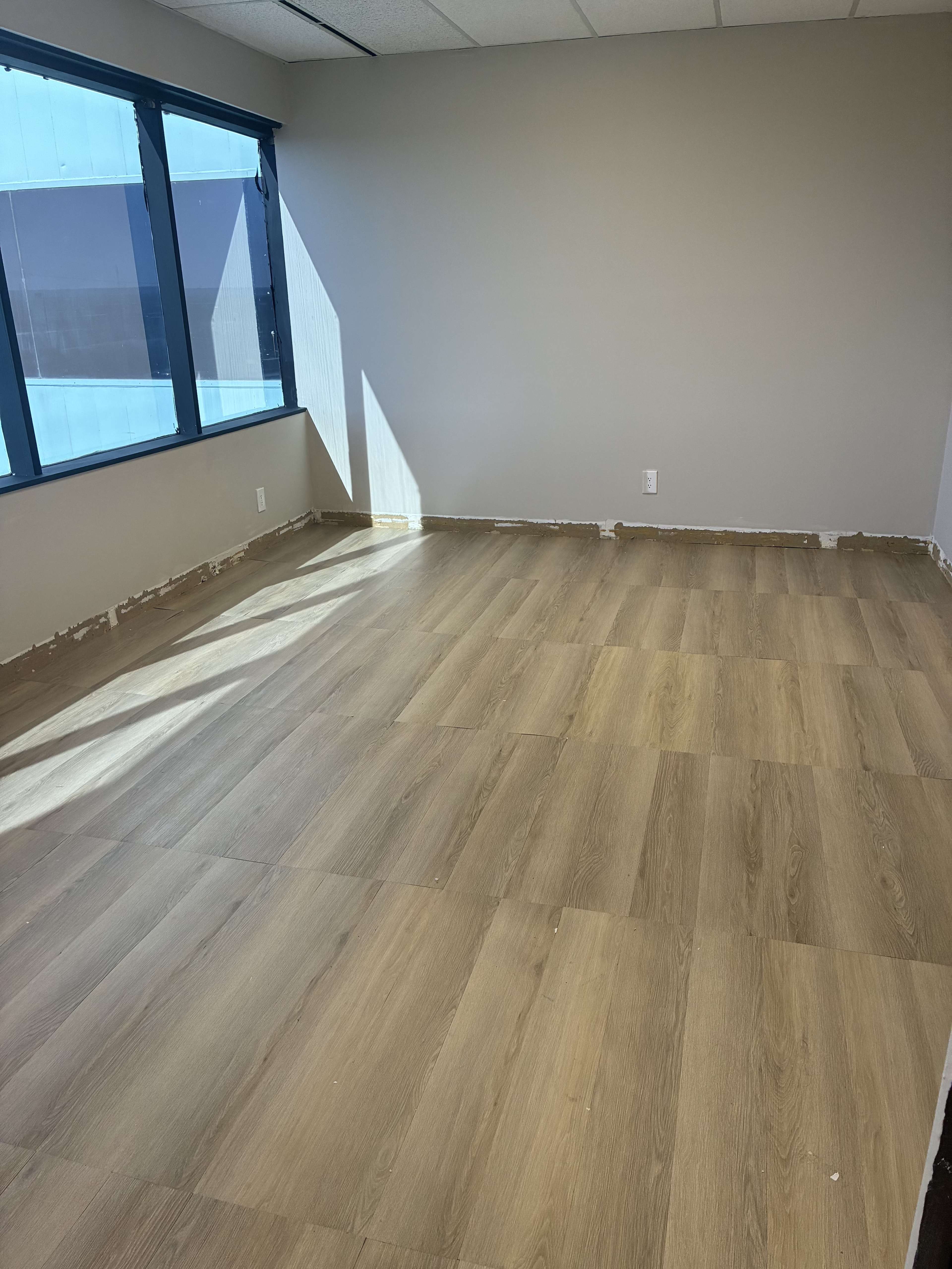 The image shows an empty room with light brown laminate flooring and partially painted walls.