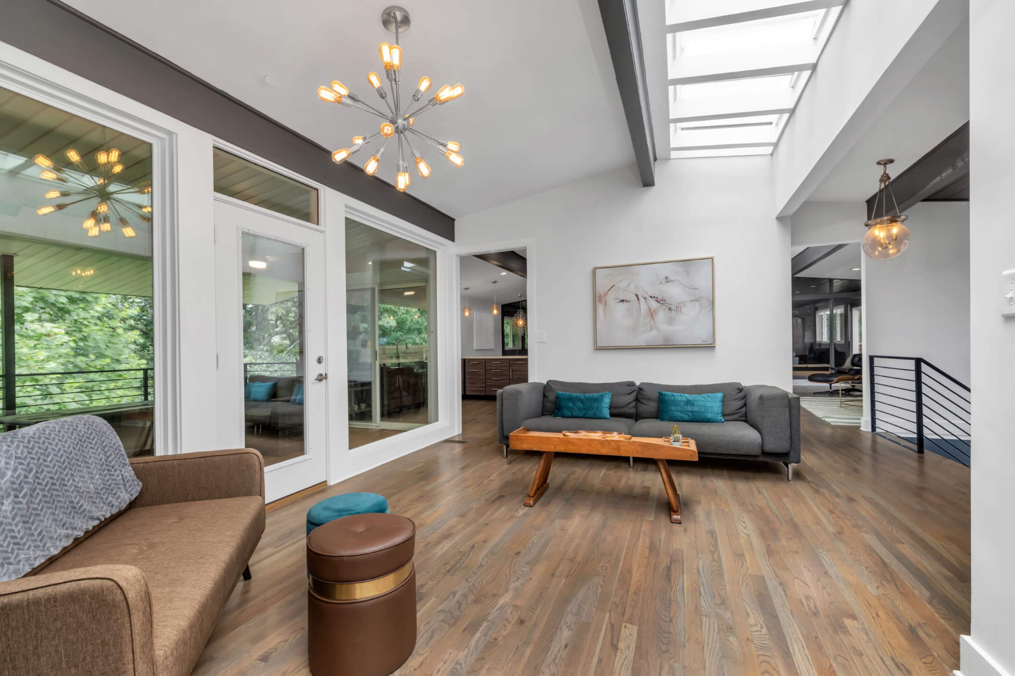 A modern living area featuring a light-filled space with large windows, wooden floors, and contemporary furniture, including a sofa and a coffee table.