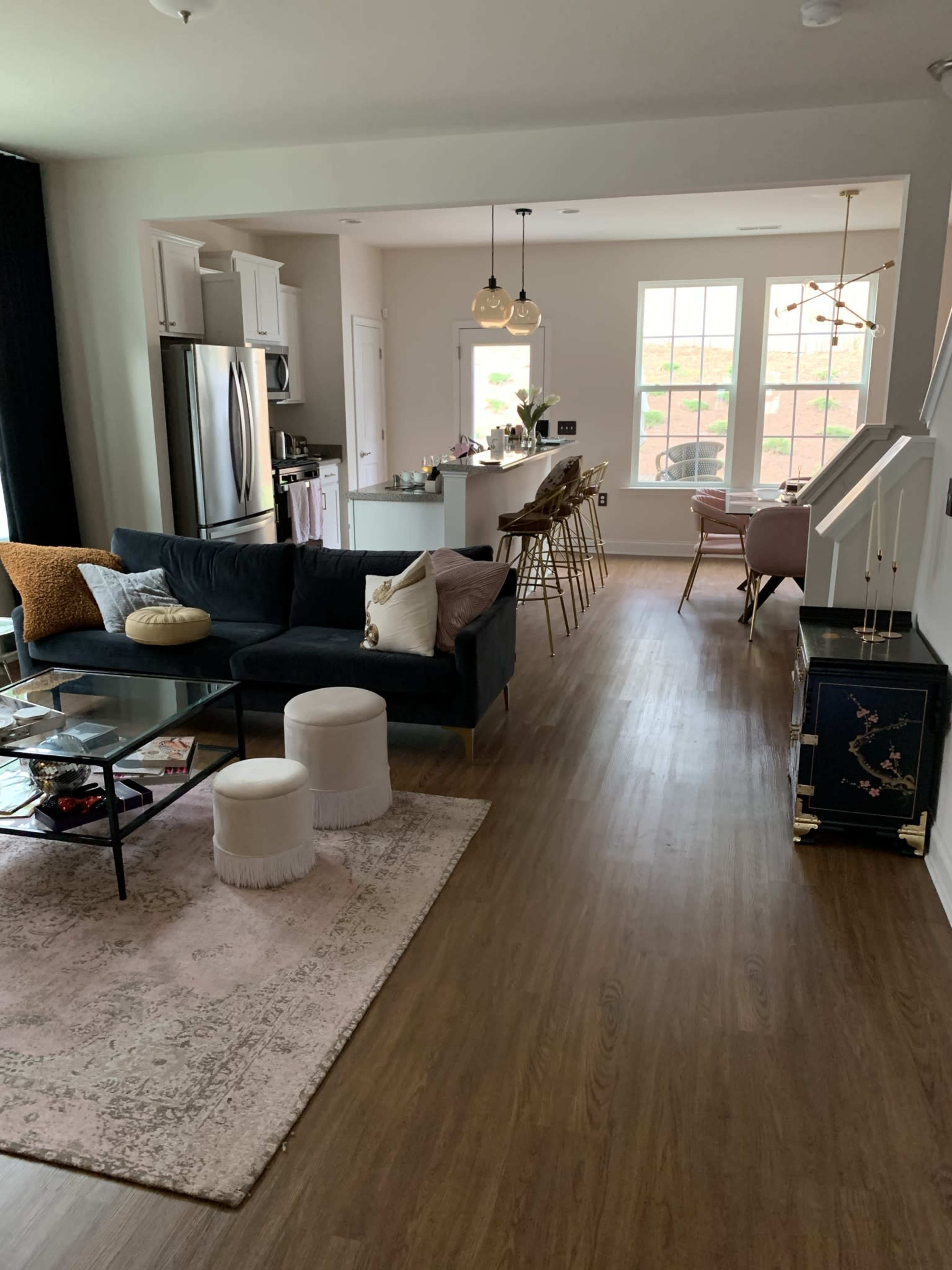 A modern open-concept living and dining area featuring a dark sofa, a glass coffee table, and a kitchen with bar stools.