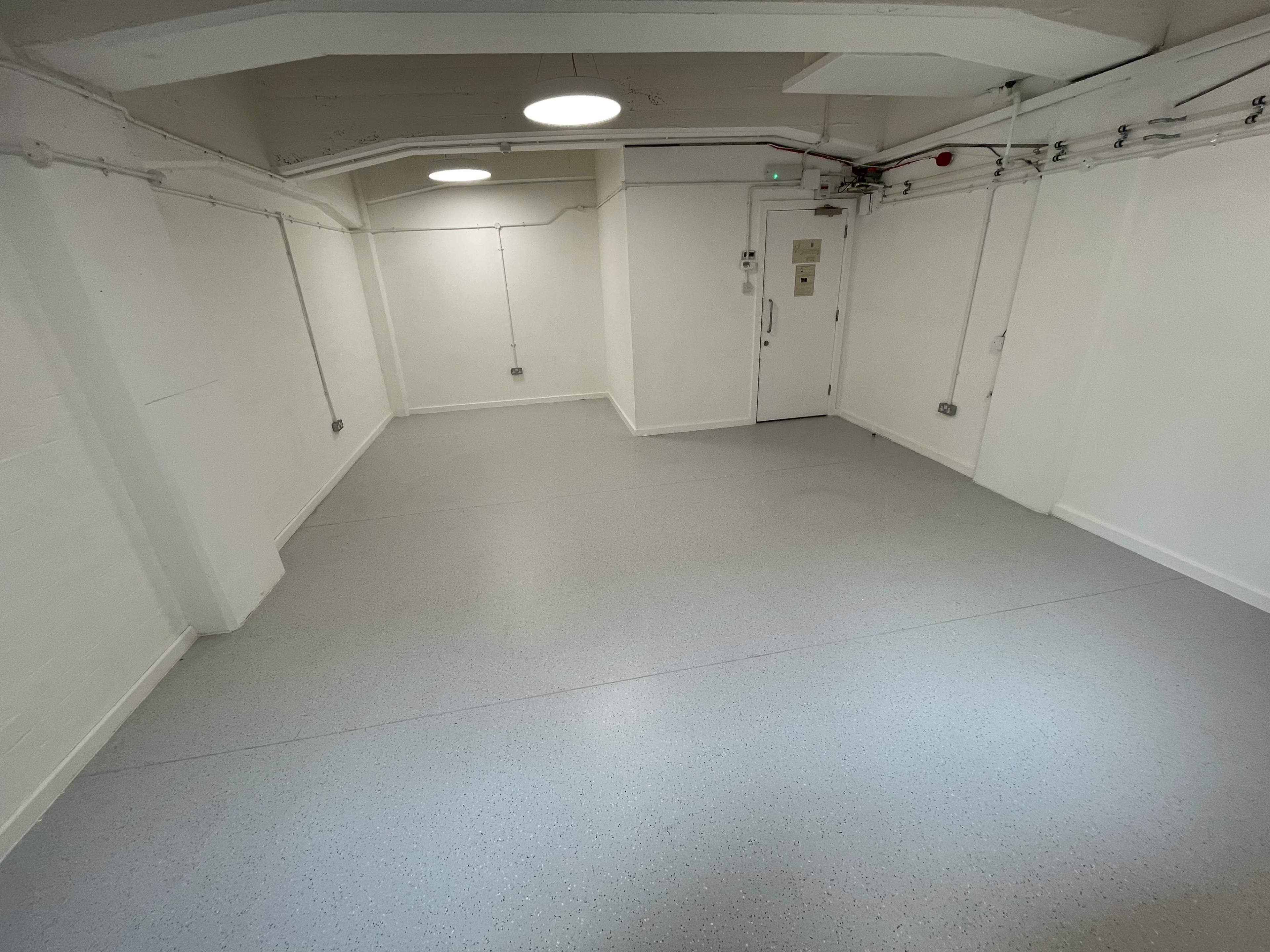 A vacant, well-lit room with plain white walls and a smooth gray floor.