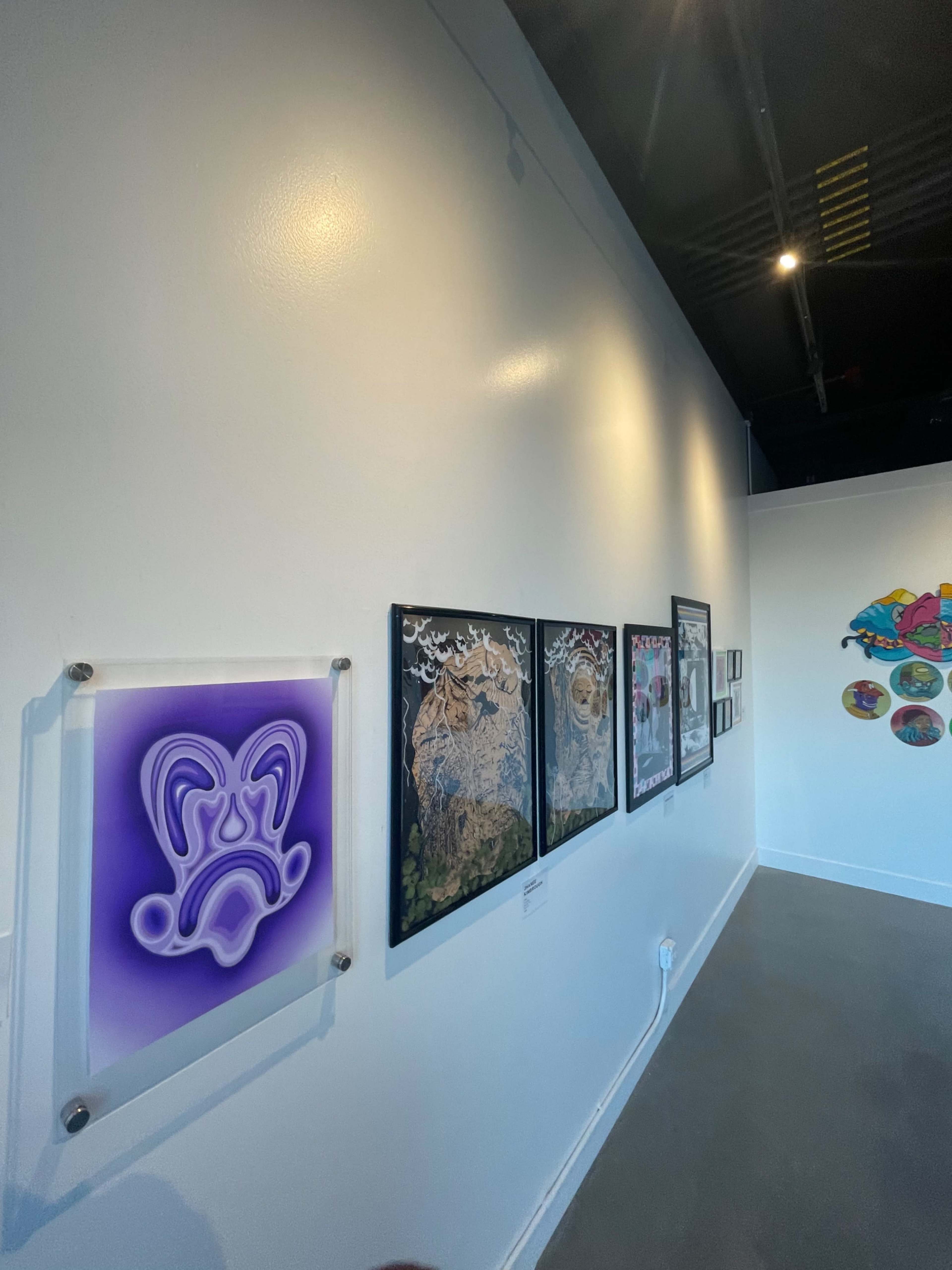 A gallery wall featuring a purple relief artwork and a series of framed artworks displayed next to it.