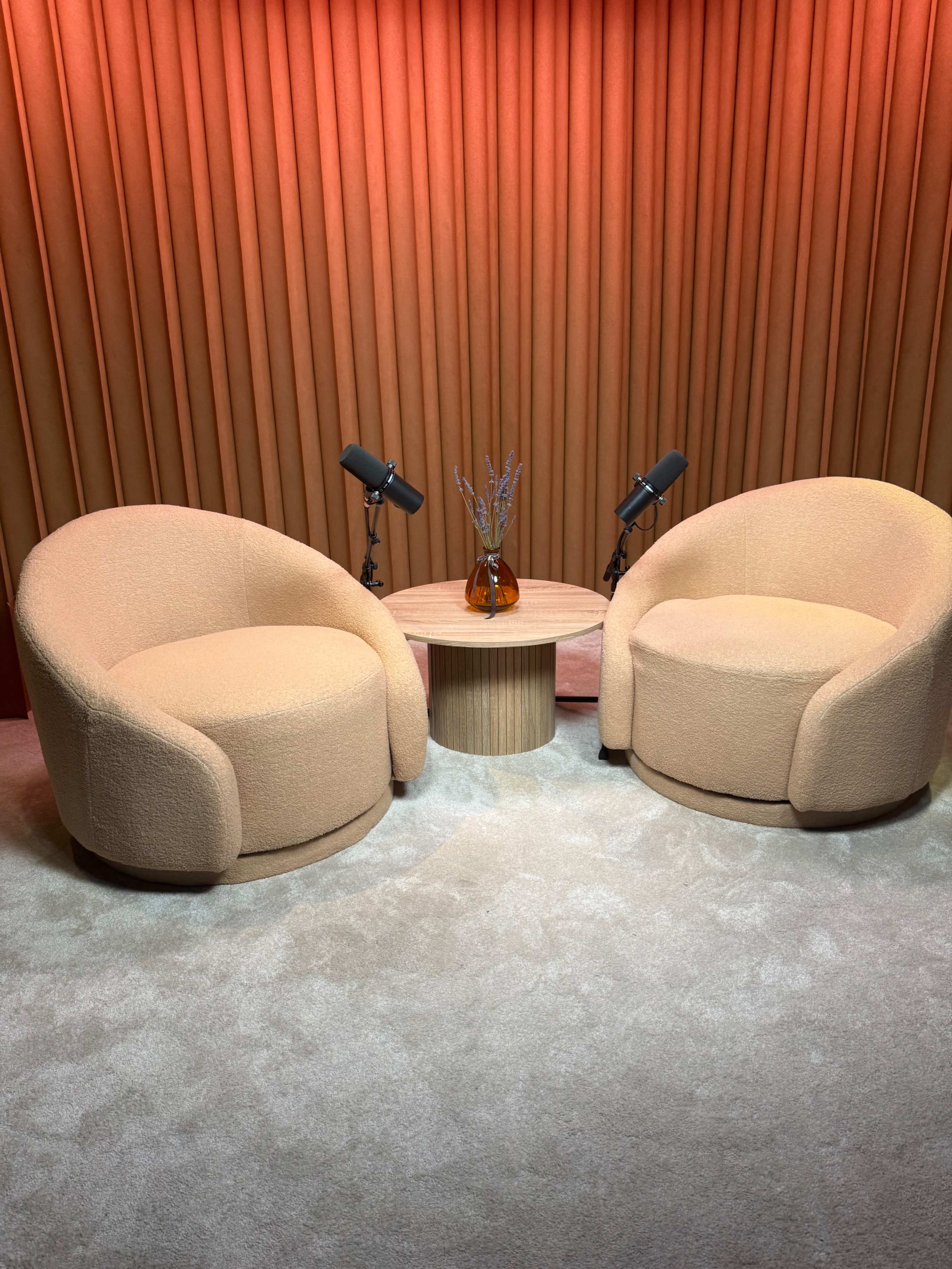 The image features two curved, beige armchairs positioned around a round table with a decorative vase in a softly lit room with orange curtains.