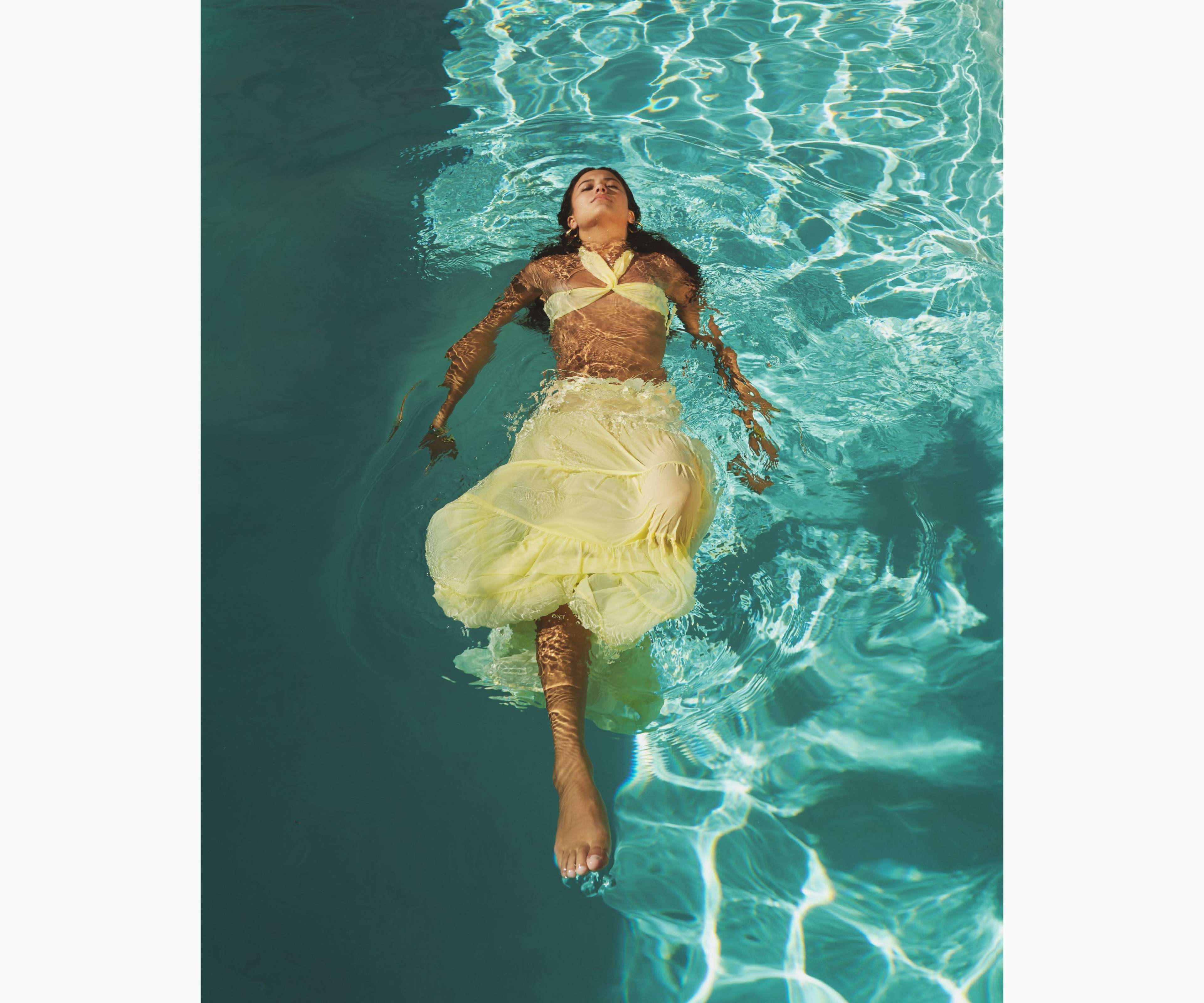 A person wearing a yellow outfit is floating on the surface of a clear blue pool.