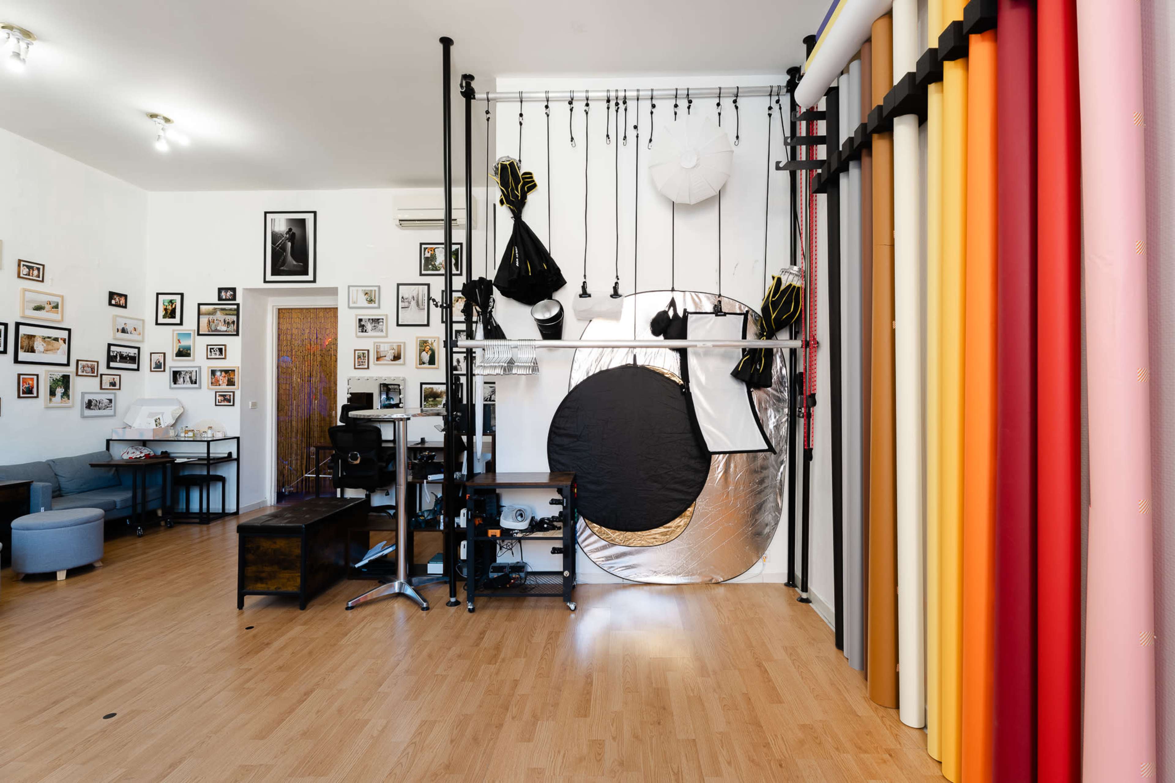 The image shows a photography studio with a backdrop setup, including various colored paper rolls, lighting equipment, and framed photographs on the walls.