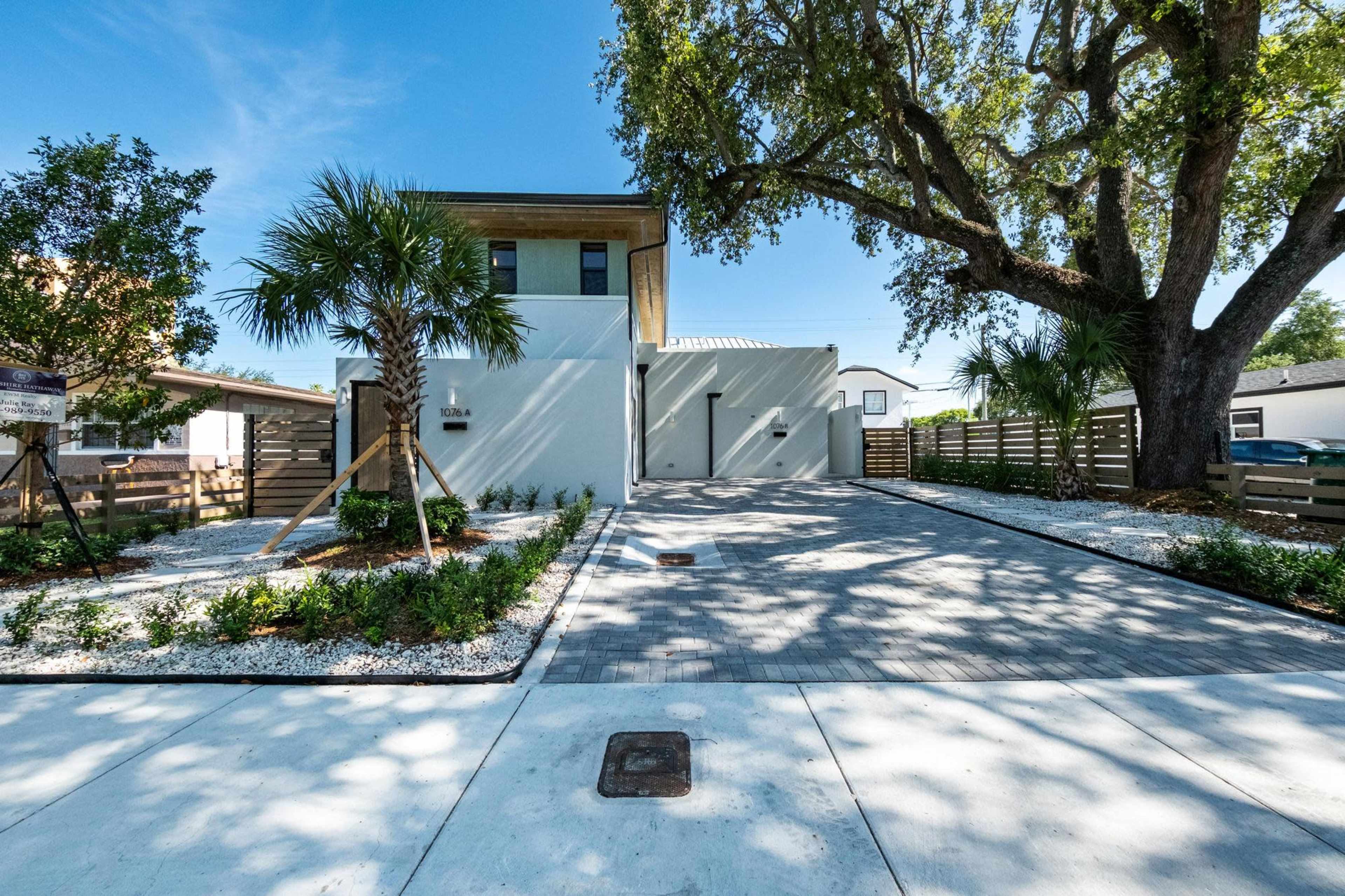The image shows a modern two-story house with a landscaped front yard featuring palm trees and a gravel driveway.