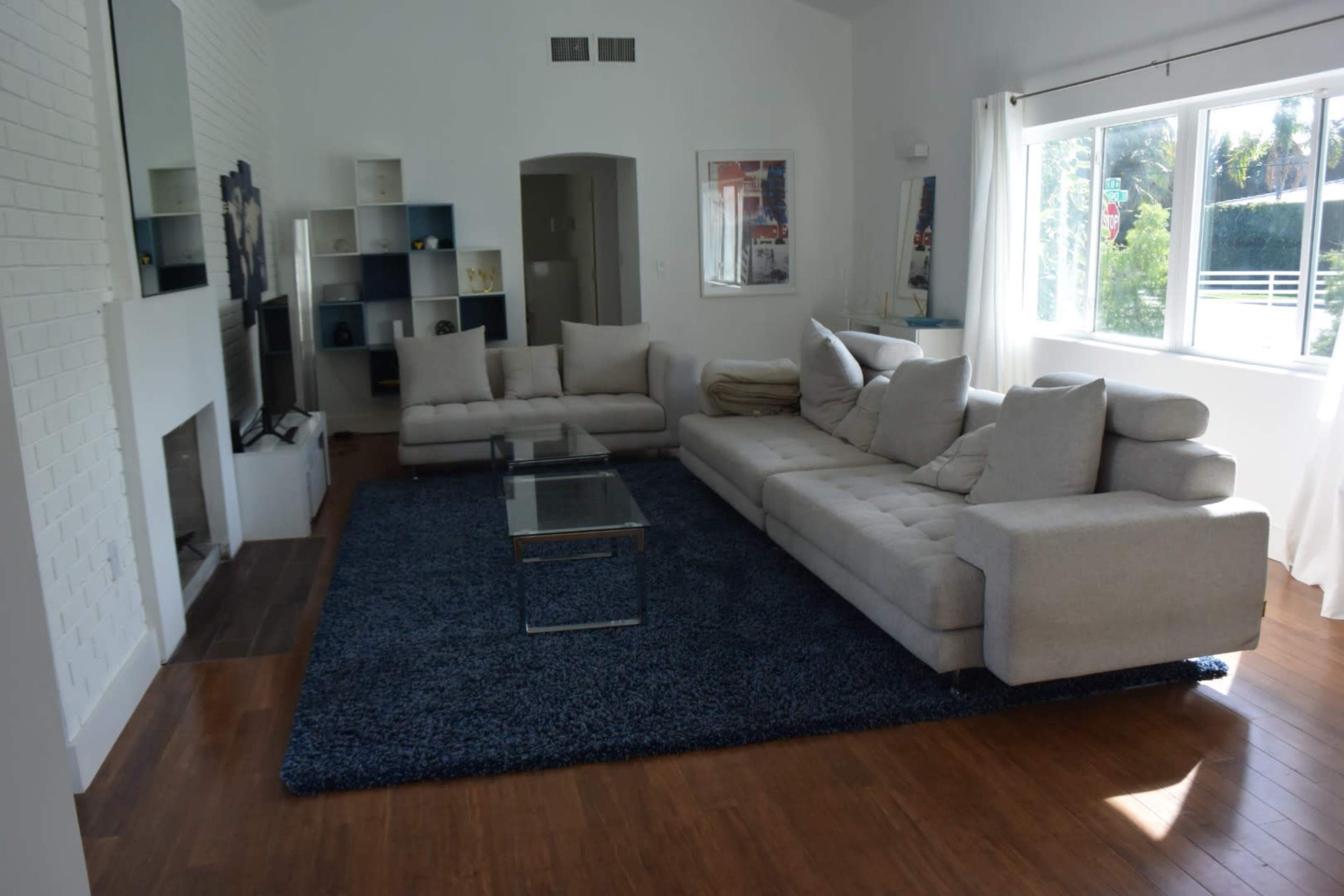 A spacious living room with a large beige sectional sofa, a glass coffee table, and a plush blue rug.