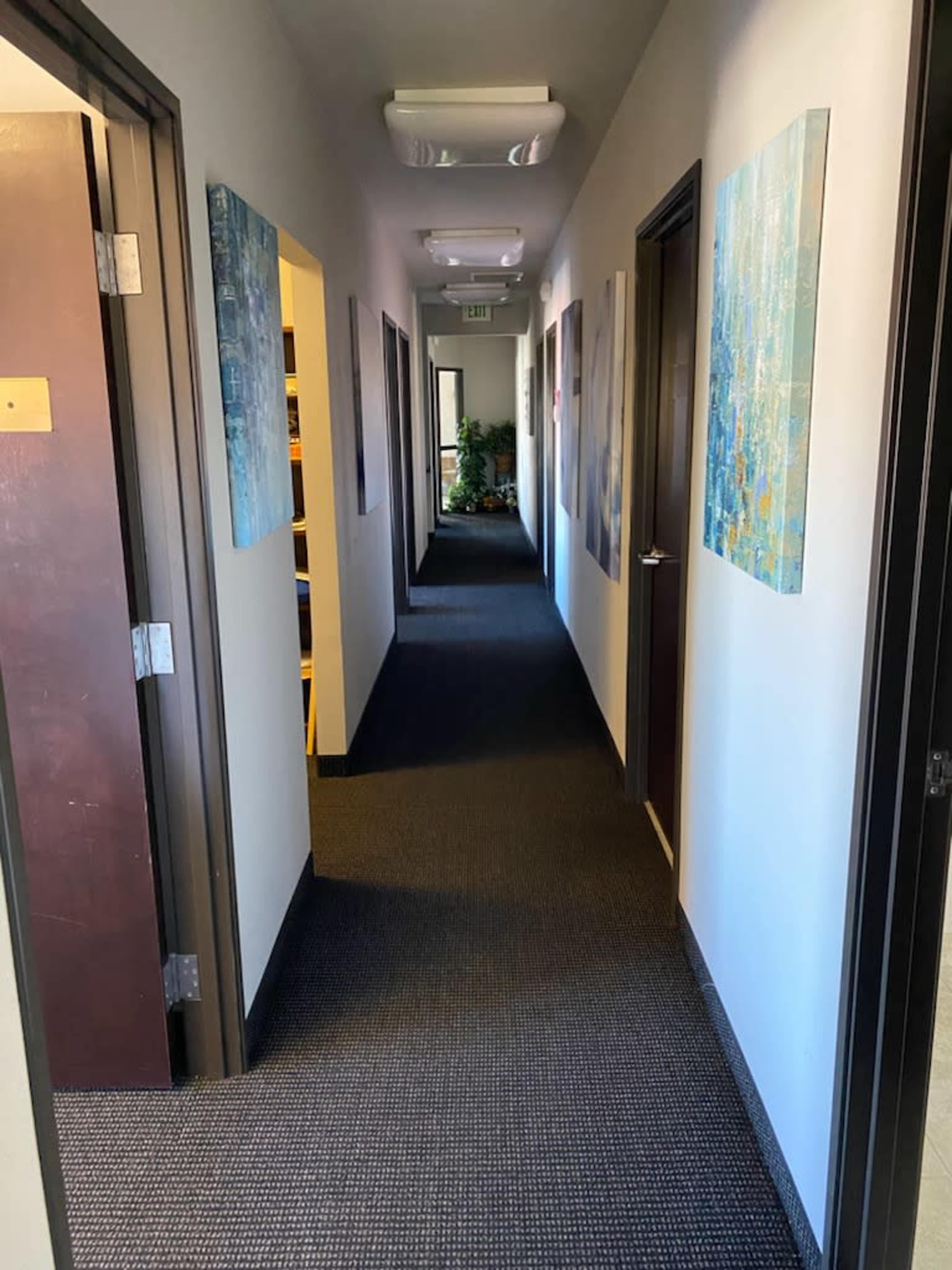 A long hallway with office doors on either side and paintings hanging on the walls.