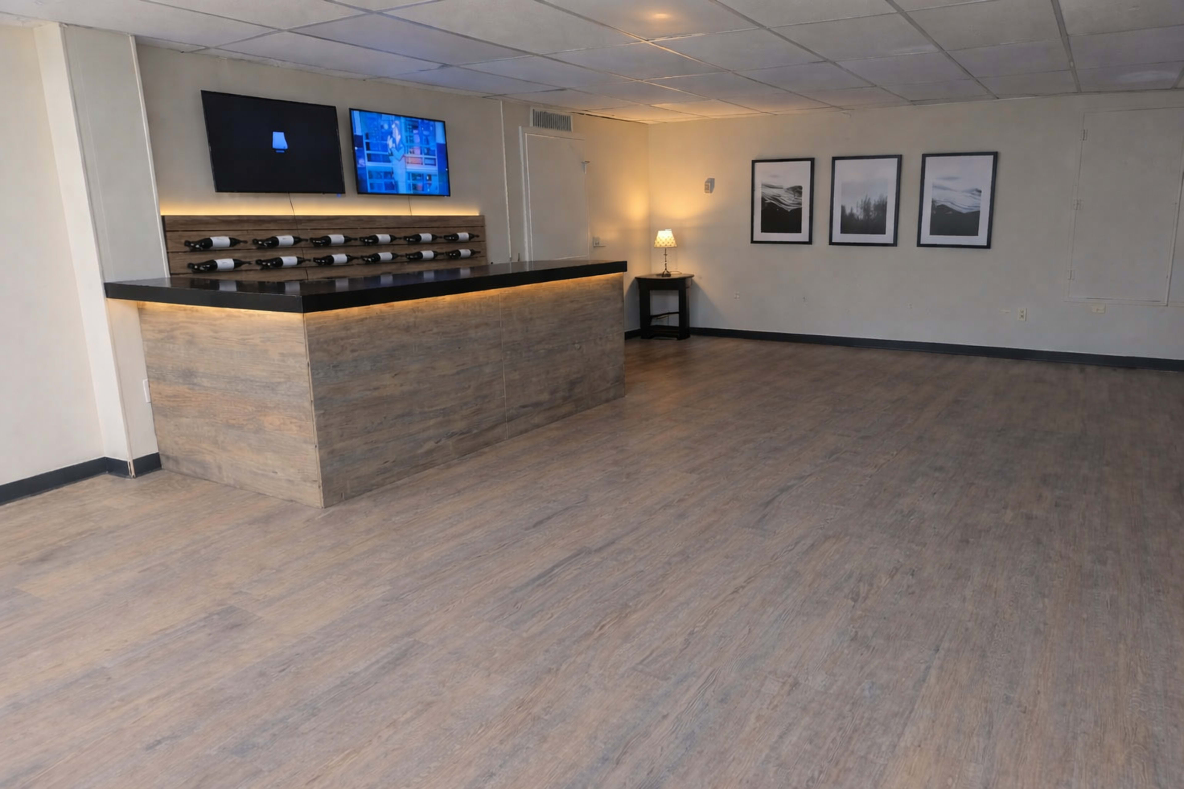 The image shows an empty room with a wooden reception counter, a wall-mounted television, and framed pictures, all set against a light-colored floor.
