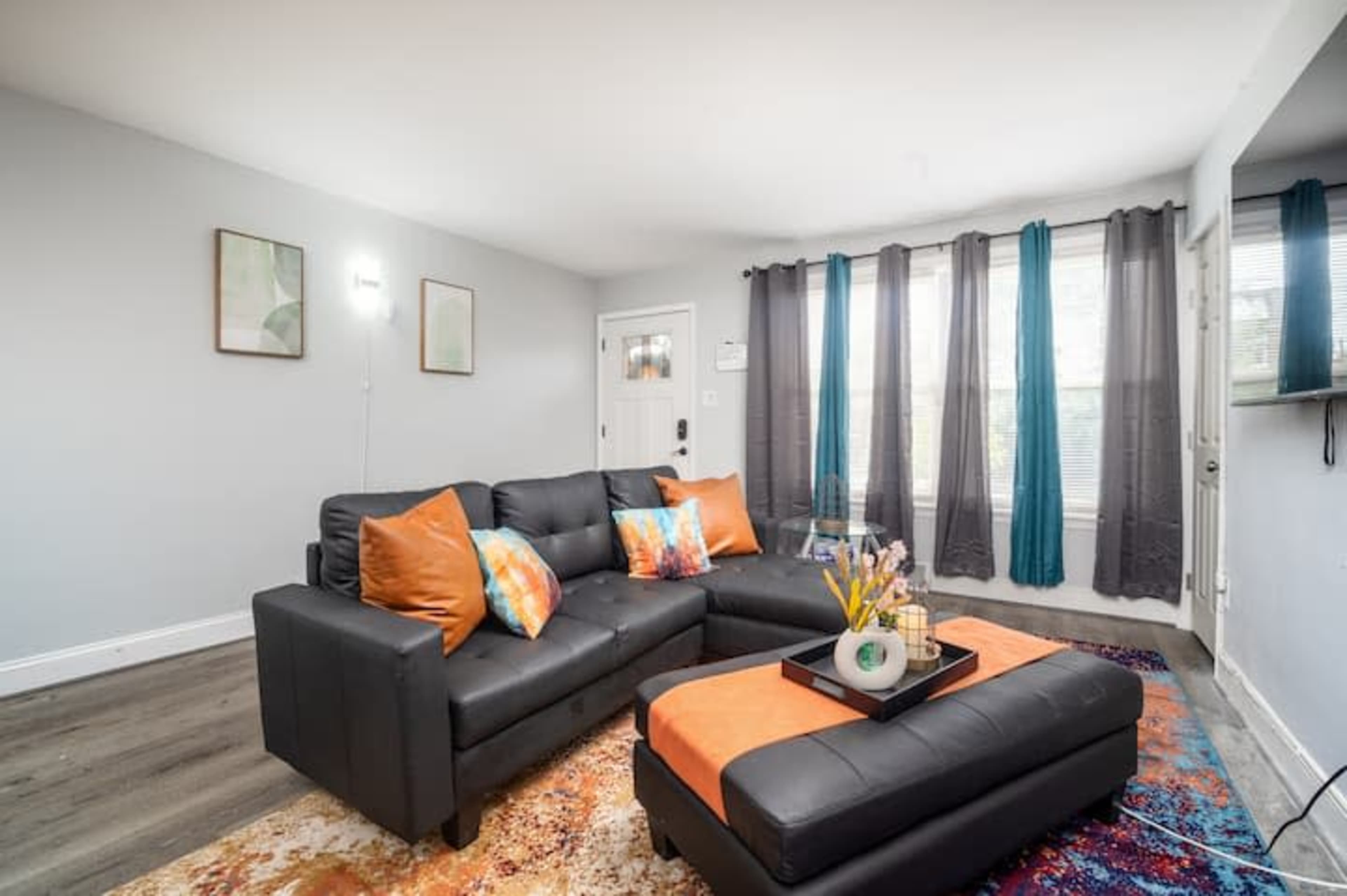 A modern living room featuring a black sectional sofa with colorful pillows, a coffee table, and large windows dressed with dark curtains.