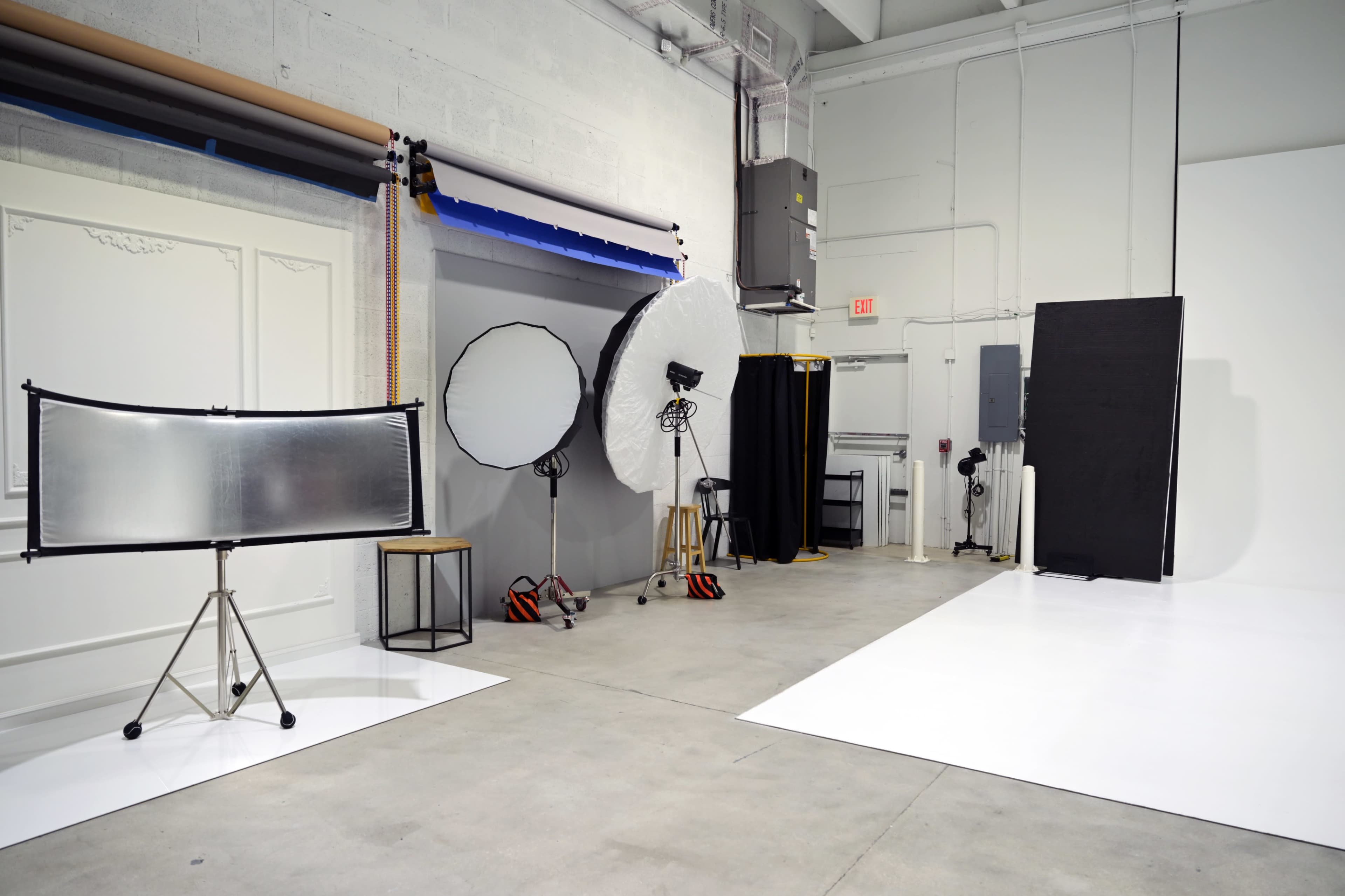 The image shows a photography studio with various lighting equipment, reflectors, and a white backdrop.