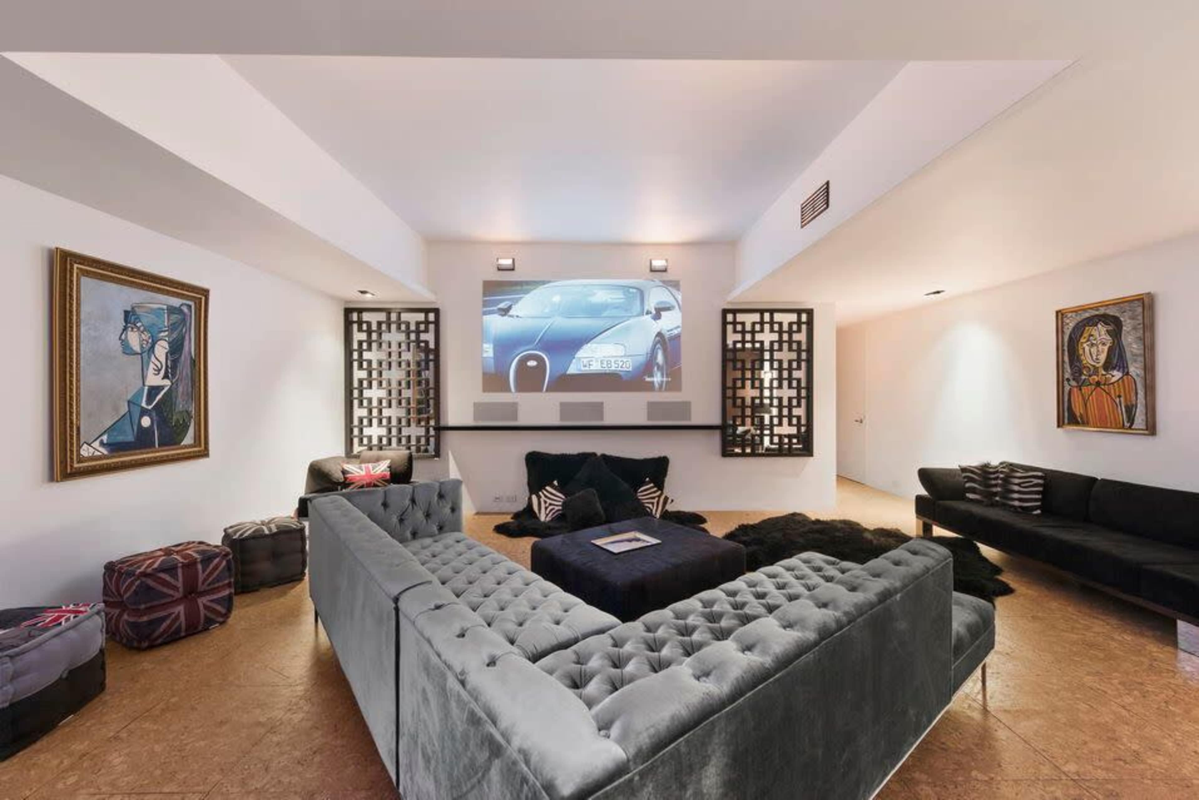 A modern living room with a large sectional sofa, artwork on the walls, and a projector displaying a car on a white screen.