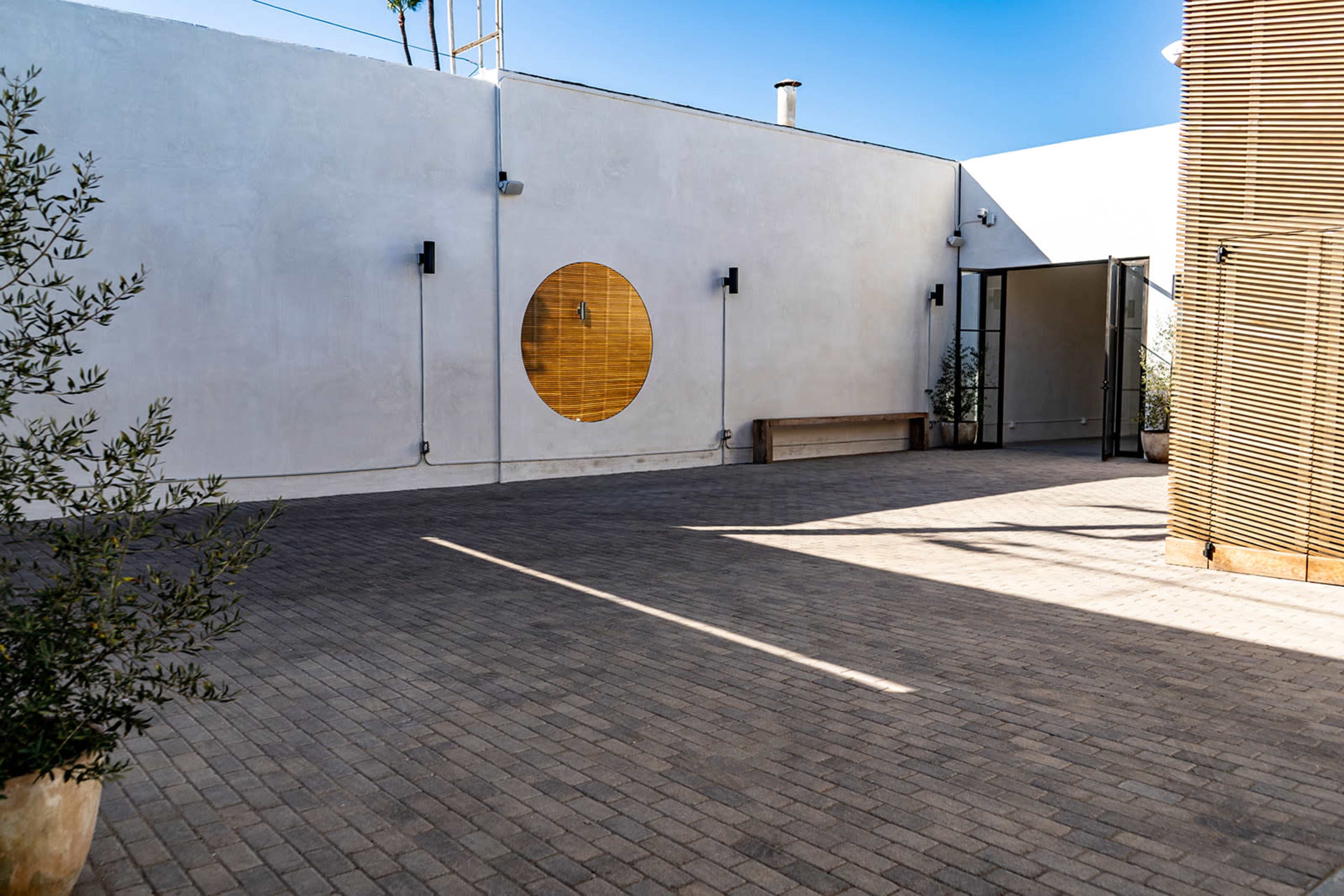 A spacious outdoor area with a textured stone surface, a large circular window on a white wall, and wooden elements along the perimeter.