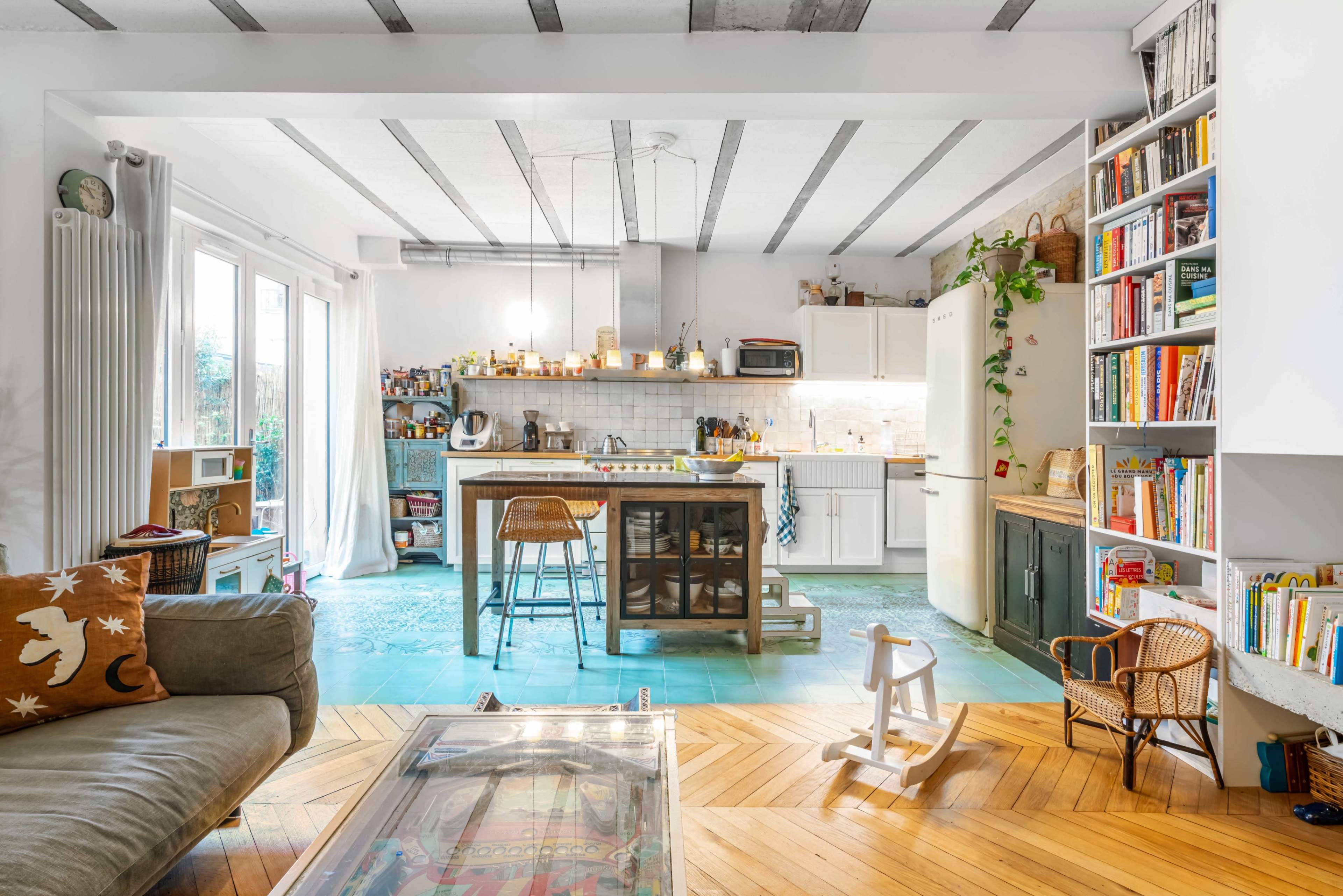 A cozy kitchen and living area with a large island, multiple bookshelves, and a mix of wooden and tiled flooring.