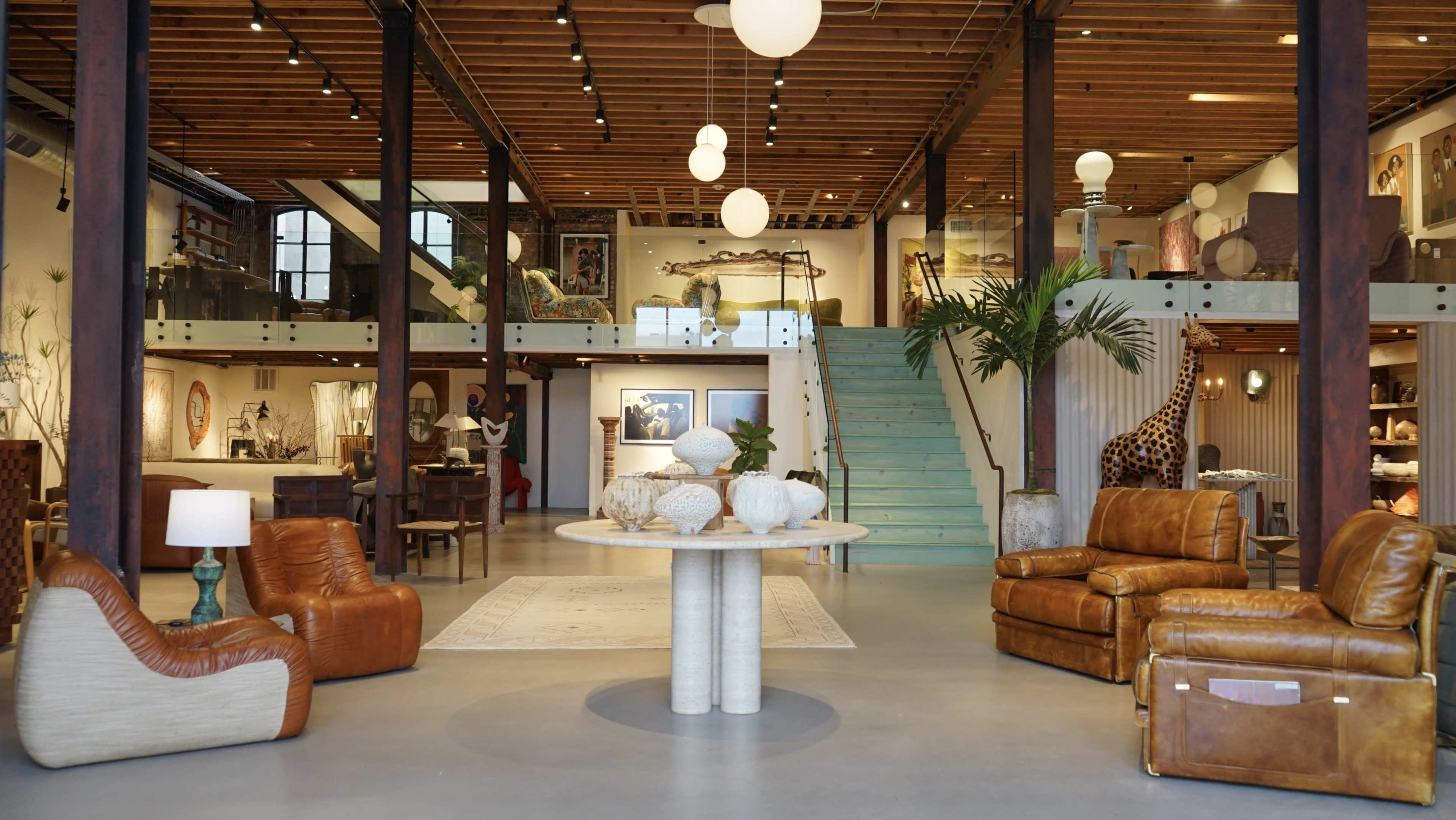 A spacious interior featuring modern furniture, a circular table with decorative vases, and a staircase leading to an upper level adorned with artwork.