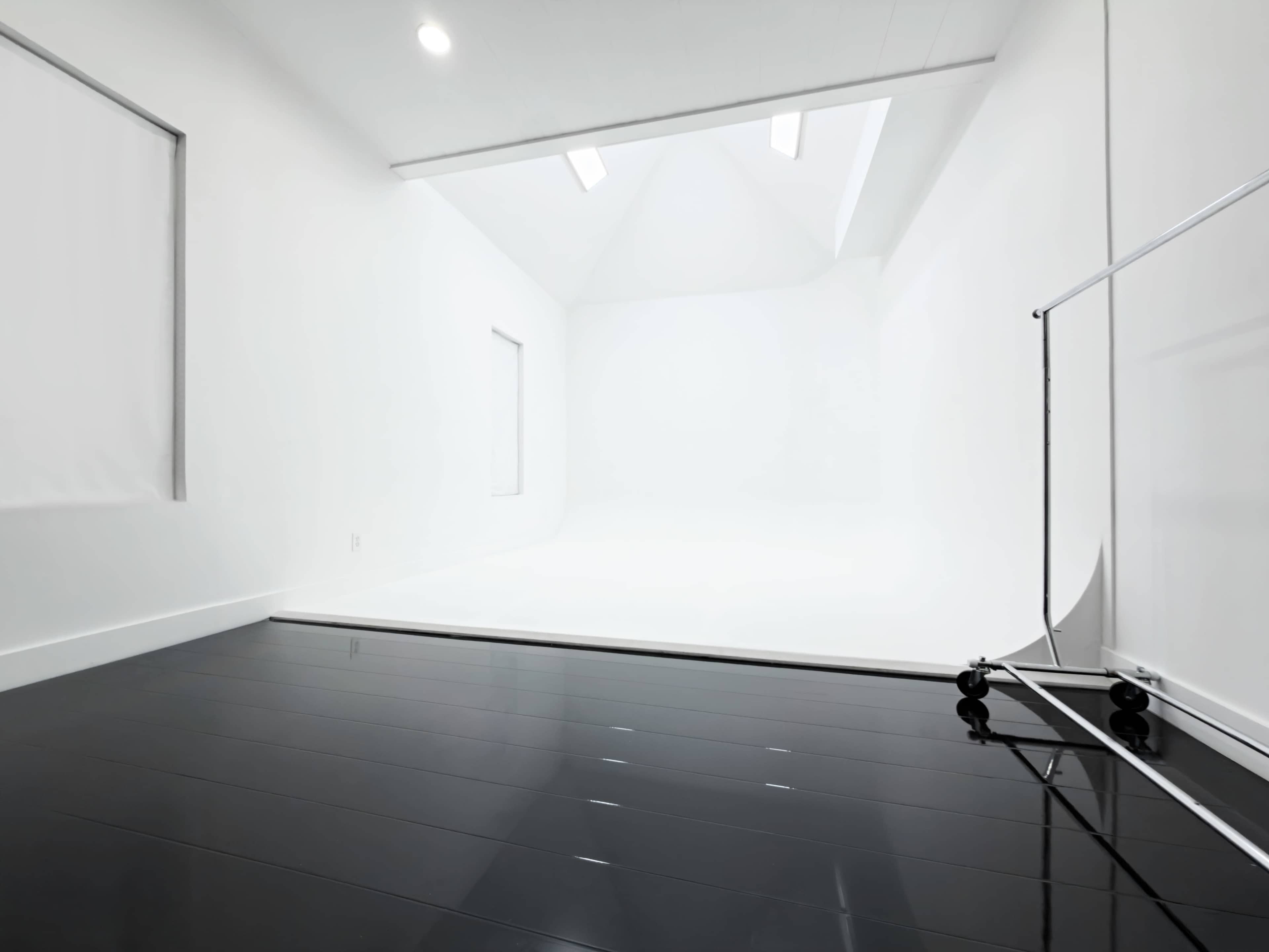 The image shows a spacious, well-lit studio with white walls, a white backdrop, and a shiny black floor.