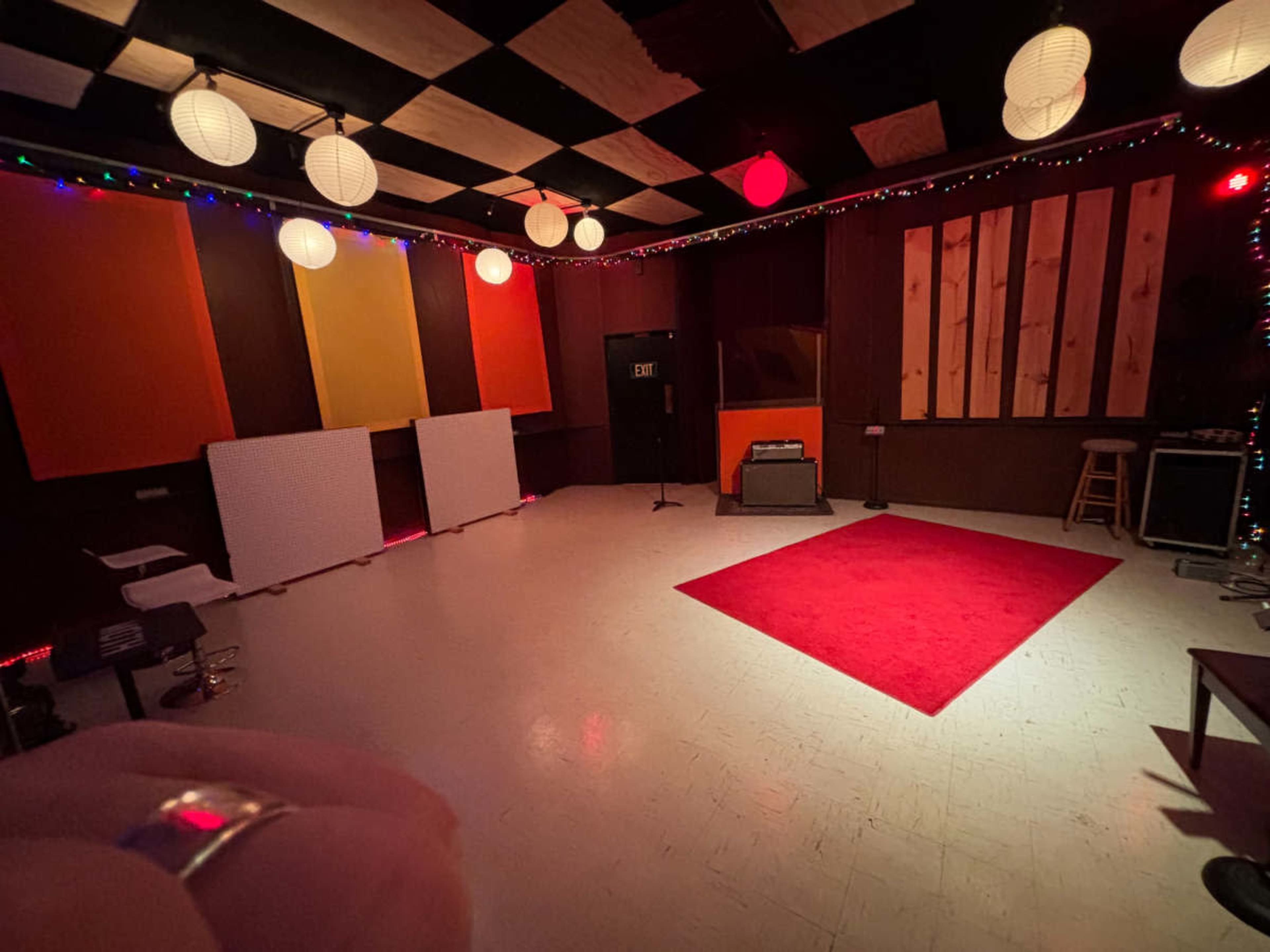 The image shows a music studio with colorful wall panels, soft lighting from lanterns, a red carpet, and various equipment arranged around the room.