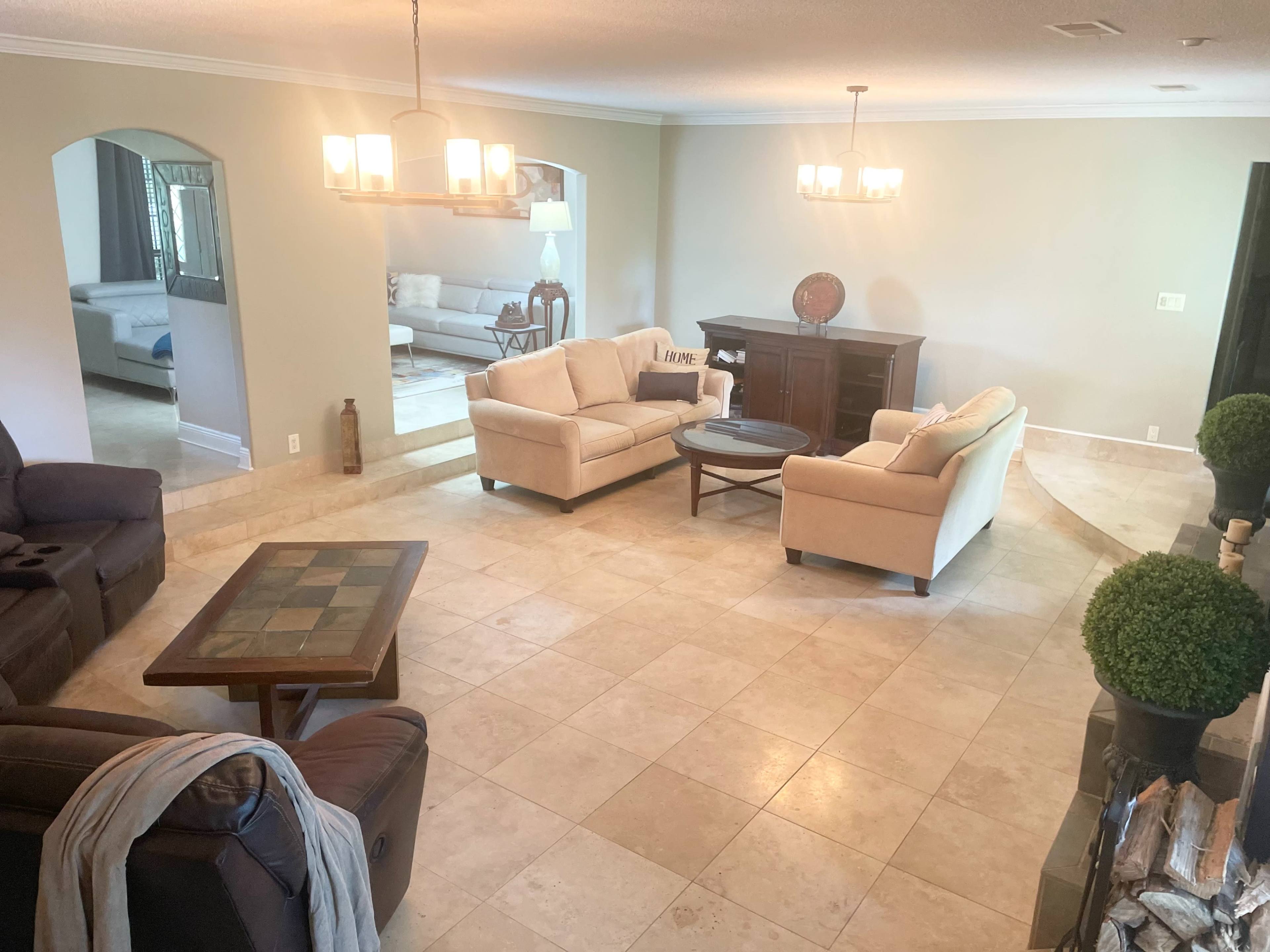 The image depicts a spacious living room with two beige sofas facing each other, a wooden coffee table in the center, and a light-colored tile floor.