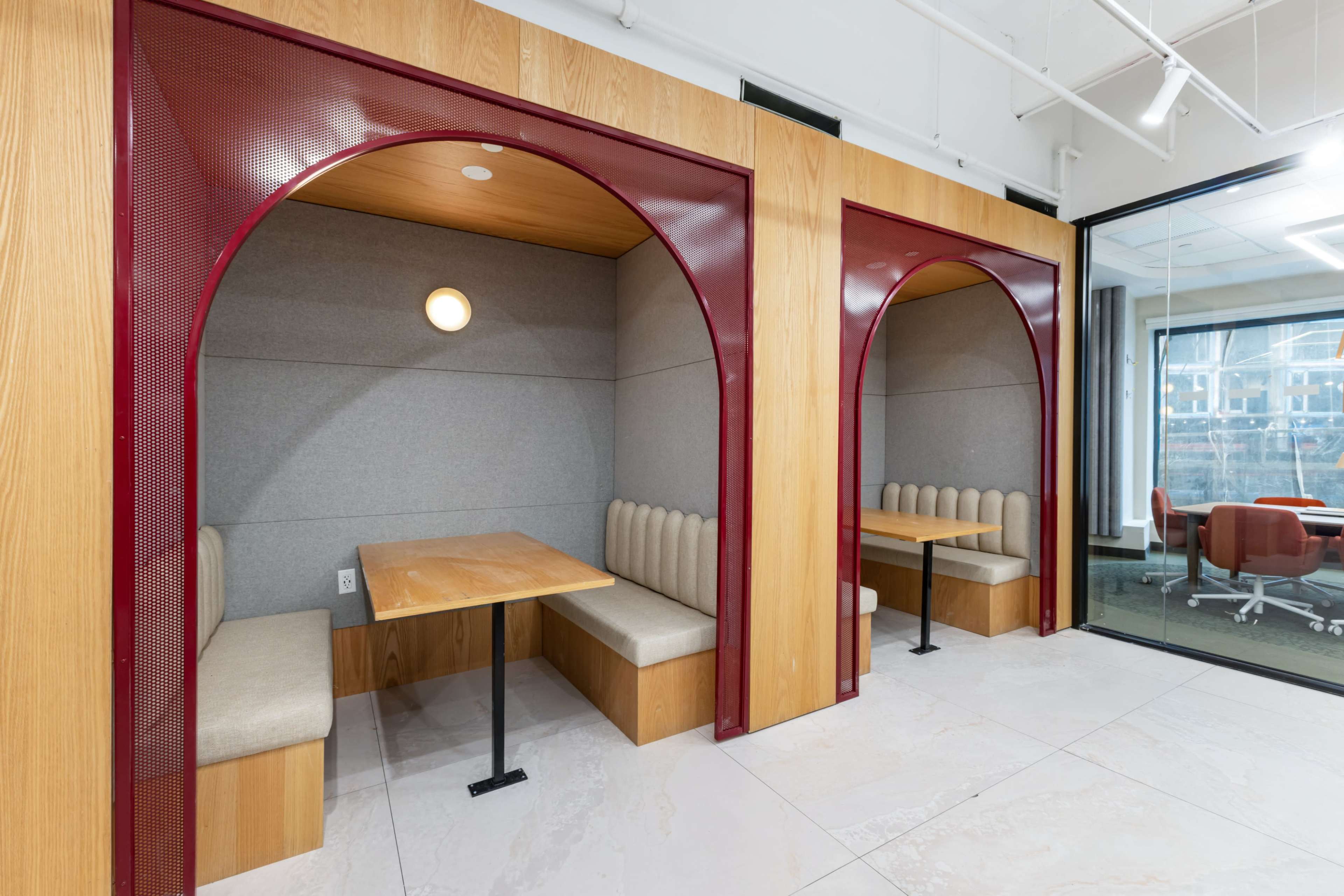 The image shows two semi-enclosed seating areas with wooden arches, each featuring a table and upholstered benches in a modern office space.
