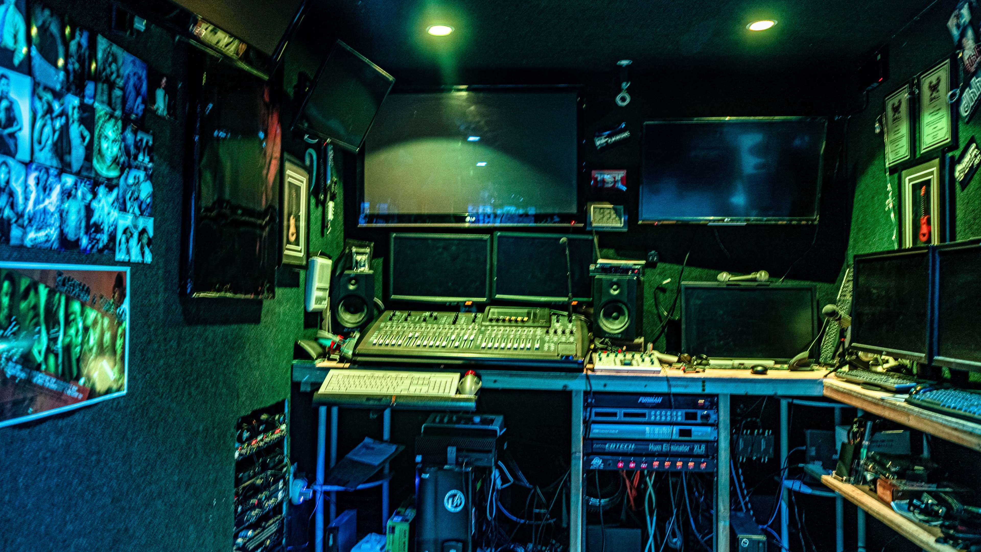 A sound studio filled with various audio equipment, multiple monitors, and an array of cables on a desk.