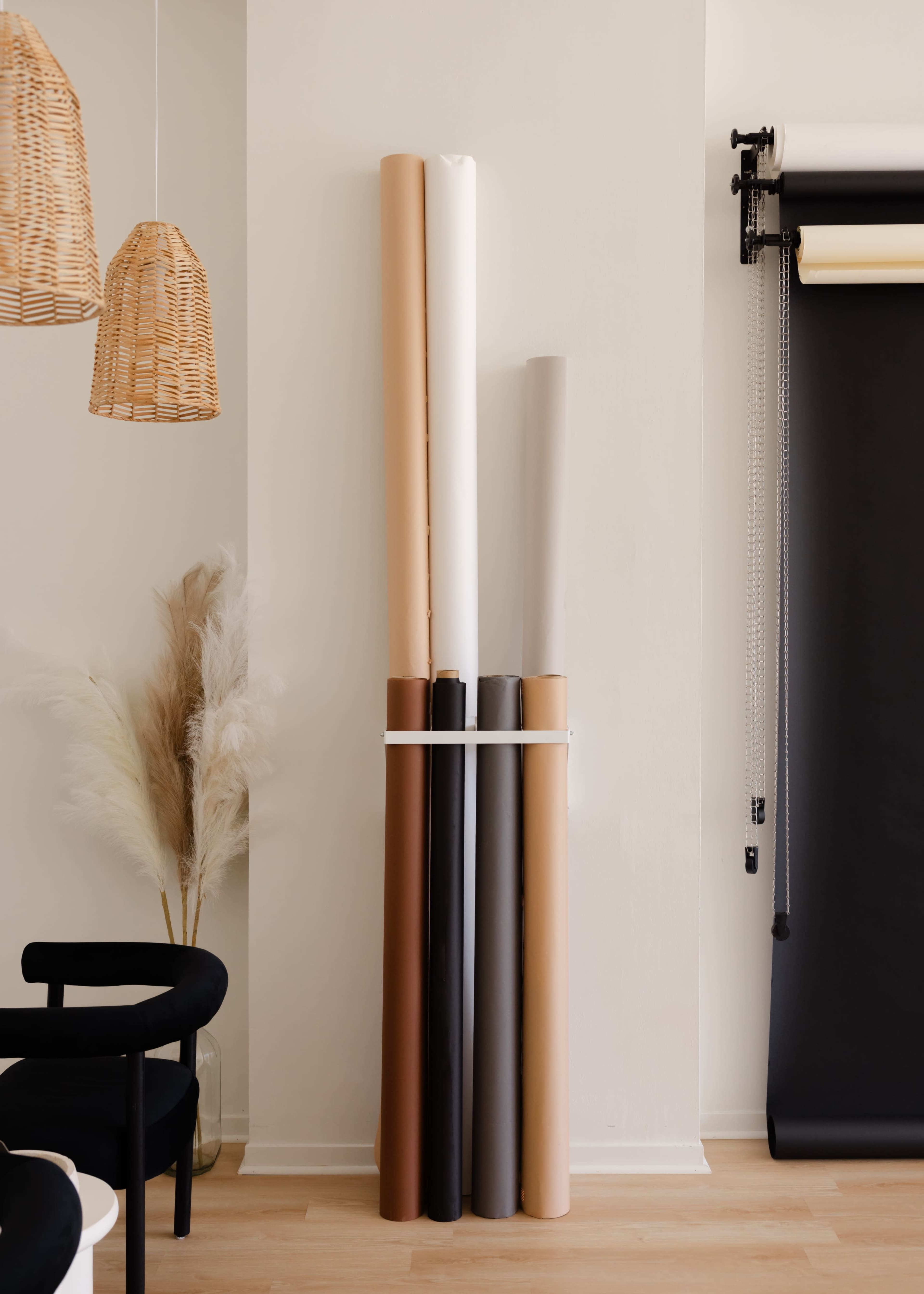 A stack of rolled paper backdrops in various colors leans against a wall, with decorative hanging lights and a plant in the background.