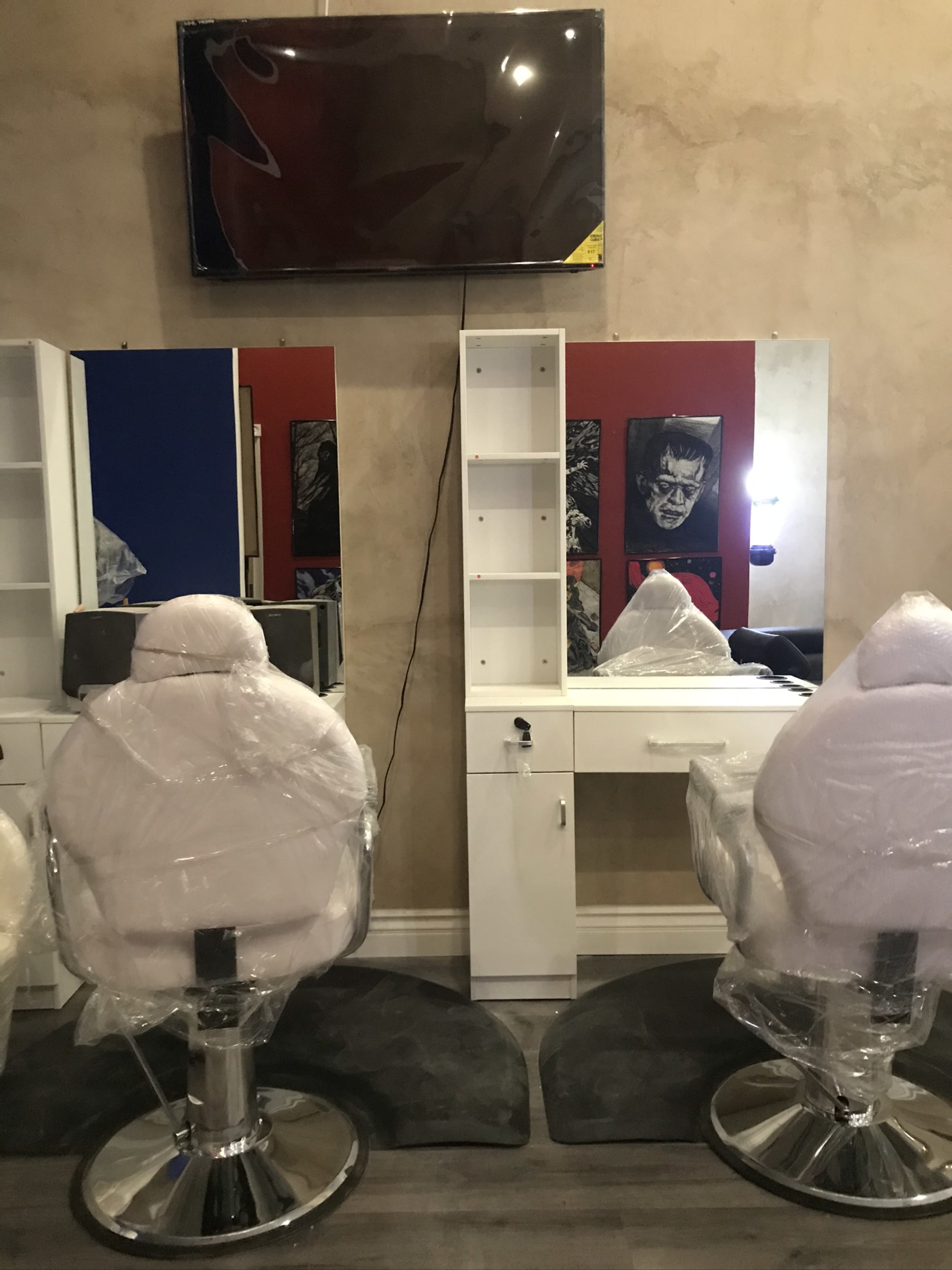 A hair salon interior with two covered styling chairs, a mirror, and a television mounted on the wall.