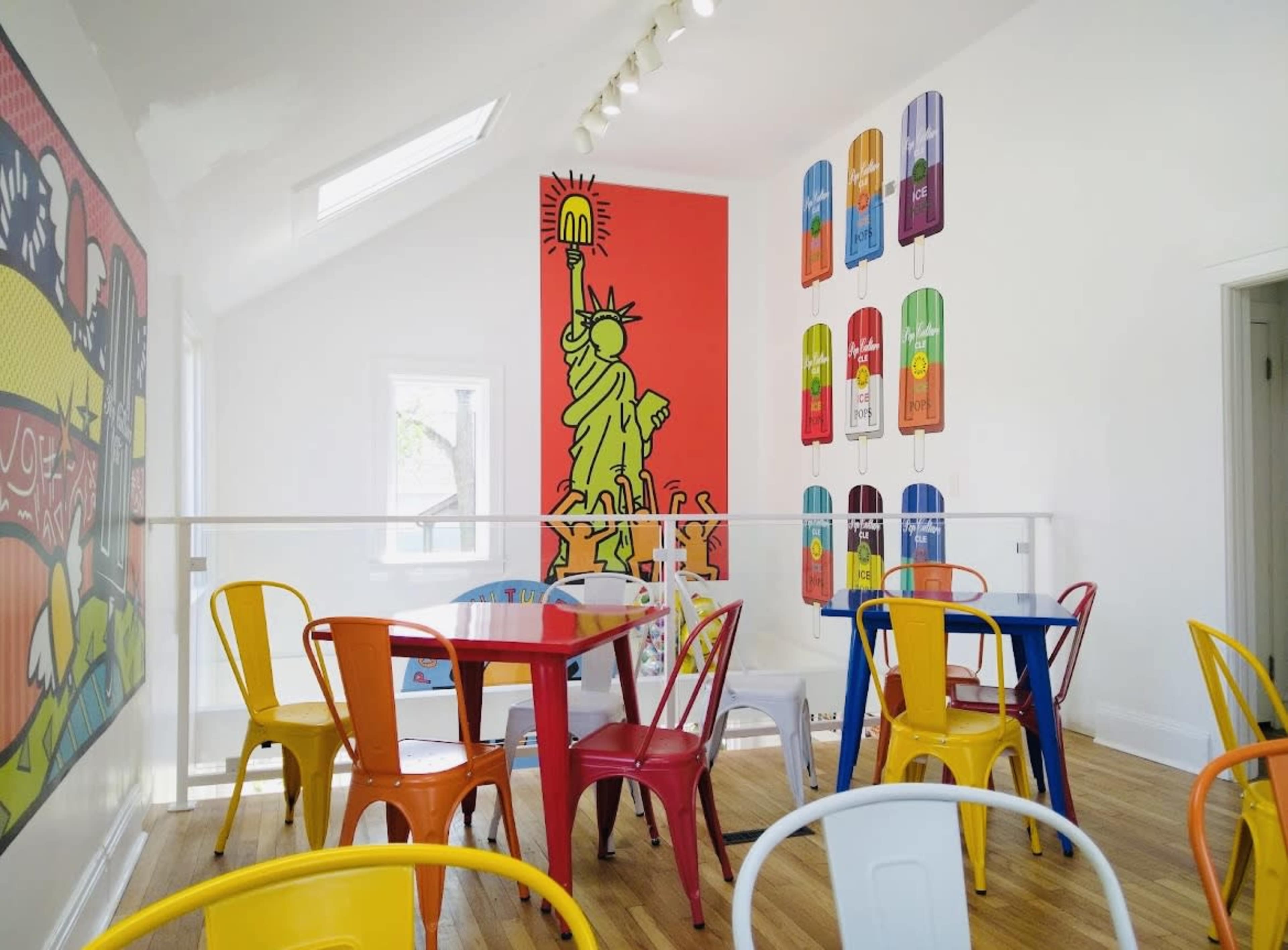 A brightly colored café interior with multicolored chairs and walls featuring graphic artwork, including a depiction of the Statue of Liberty.