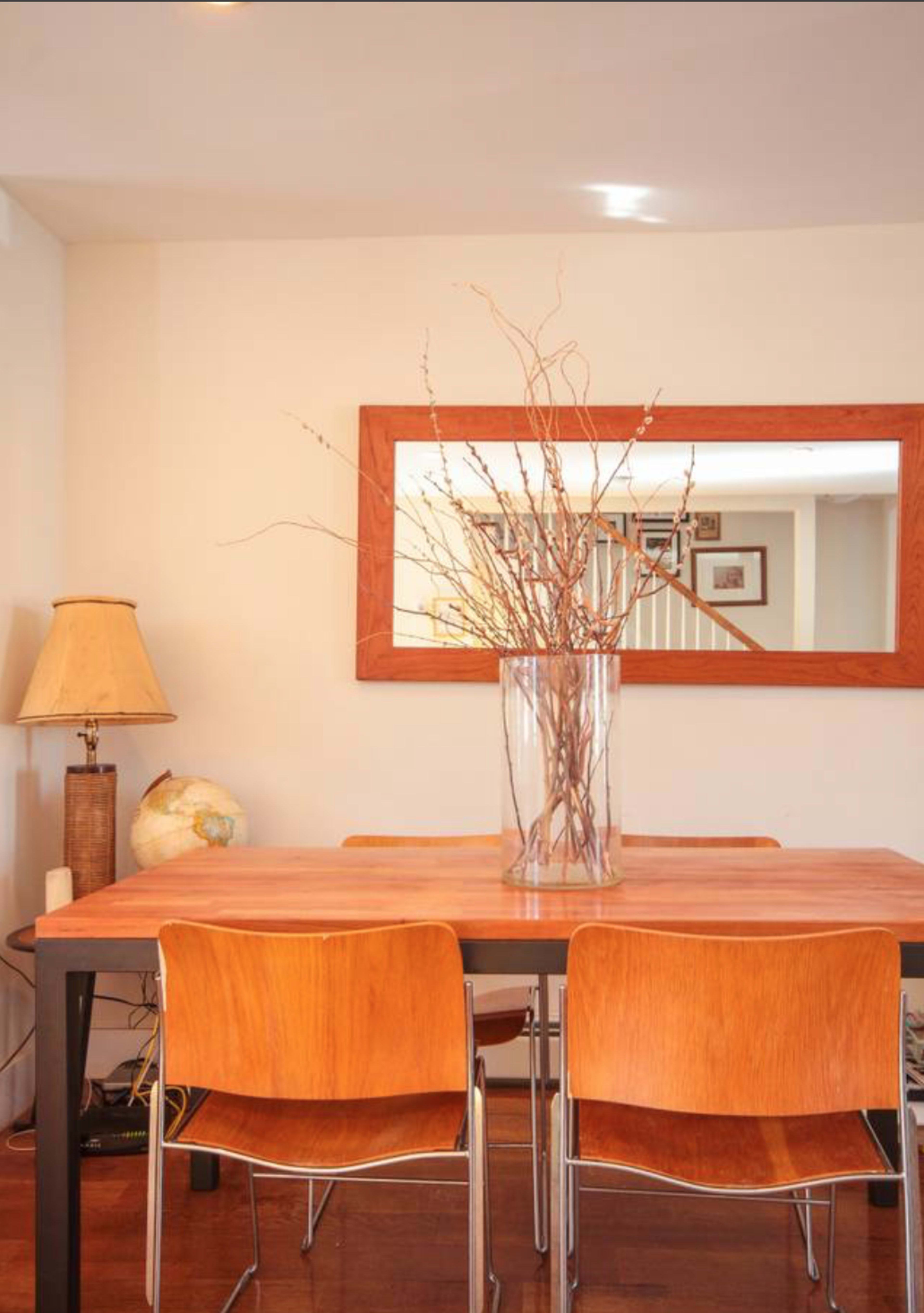 A wooden dining table with two chairs is set in a room featuring a tall vase with branches and a lamp beside a globe.