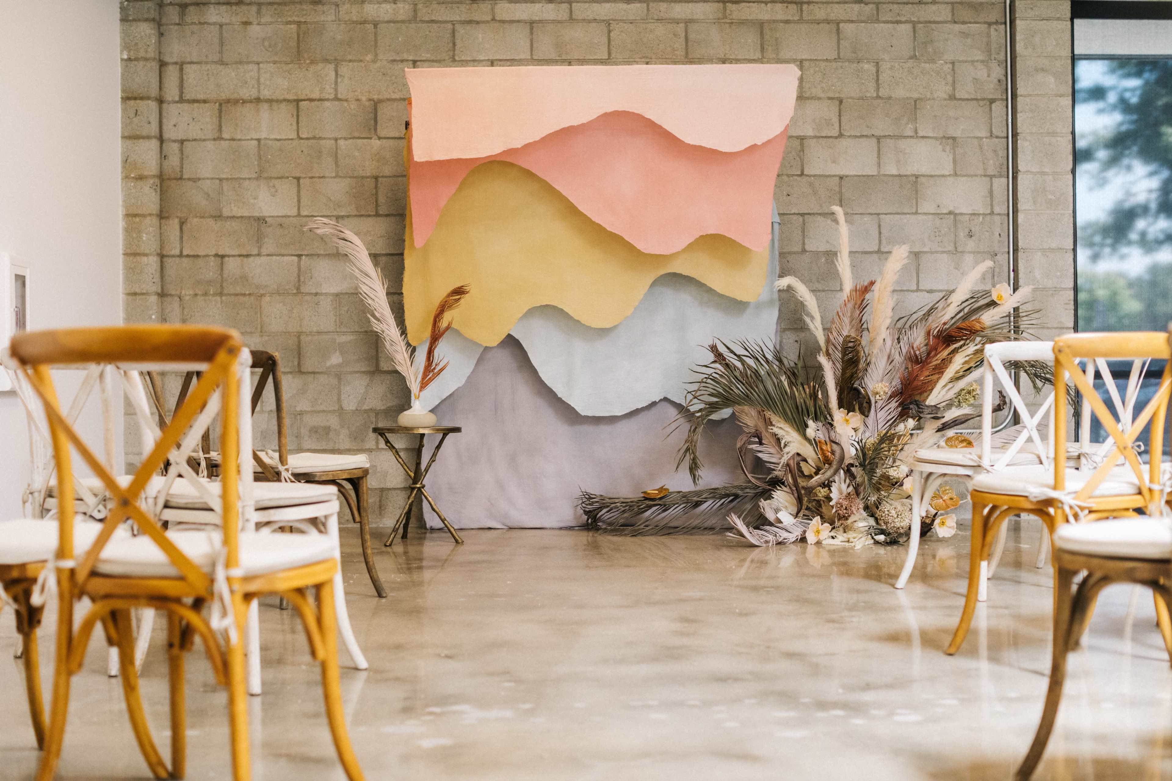 The scene features a minimalist interior setting with wooden chairs arranged in front of a colorful backdrop and floral decorations on the floor.