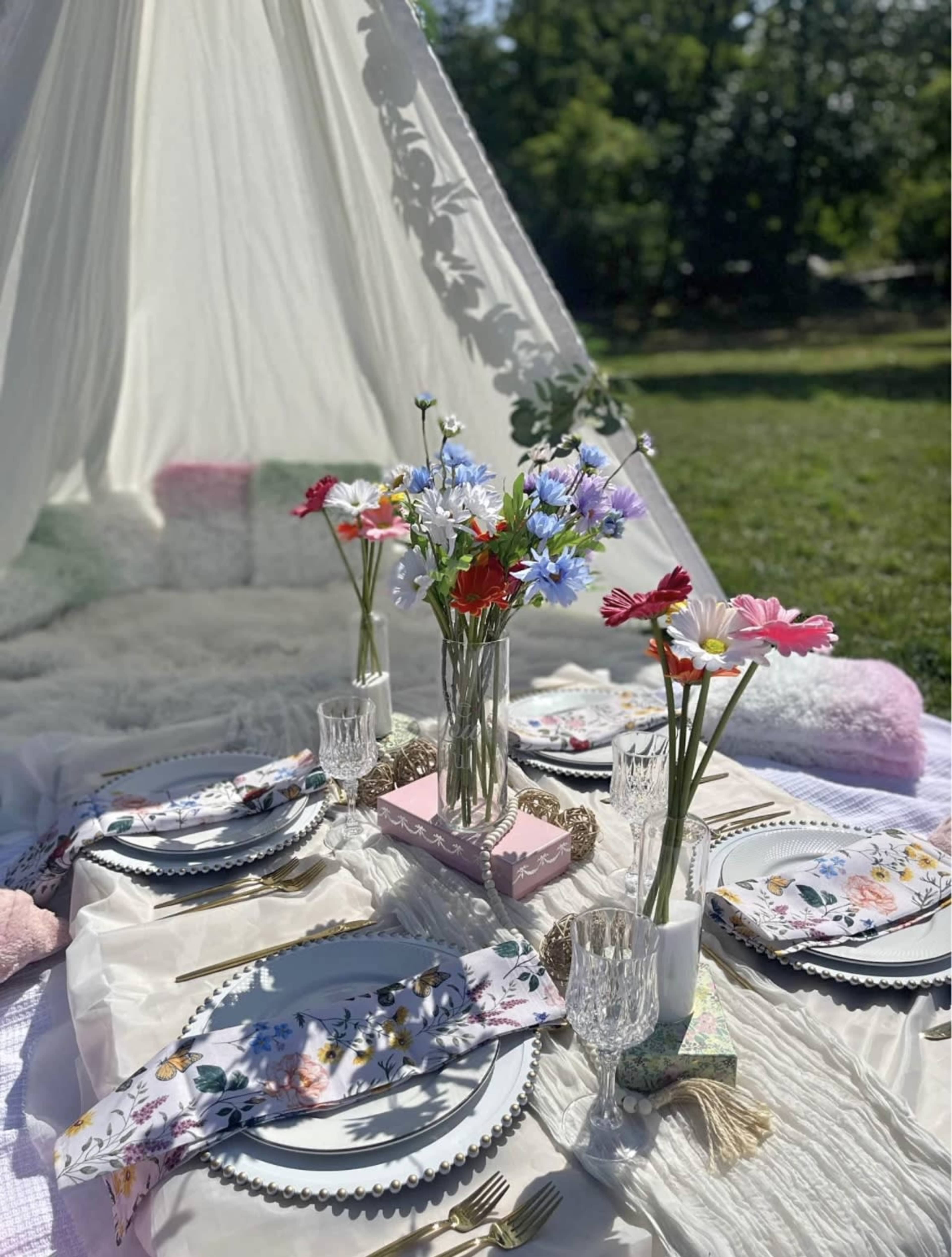 A picnic setup features a tent with floral arrangements on a blanket and decorated plates.